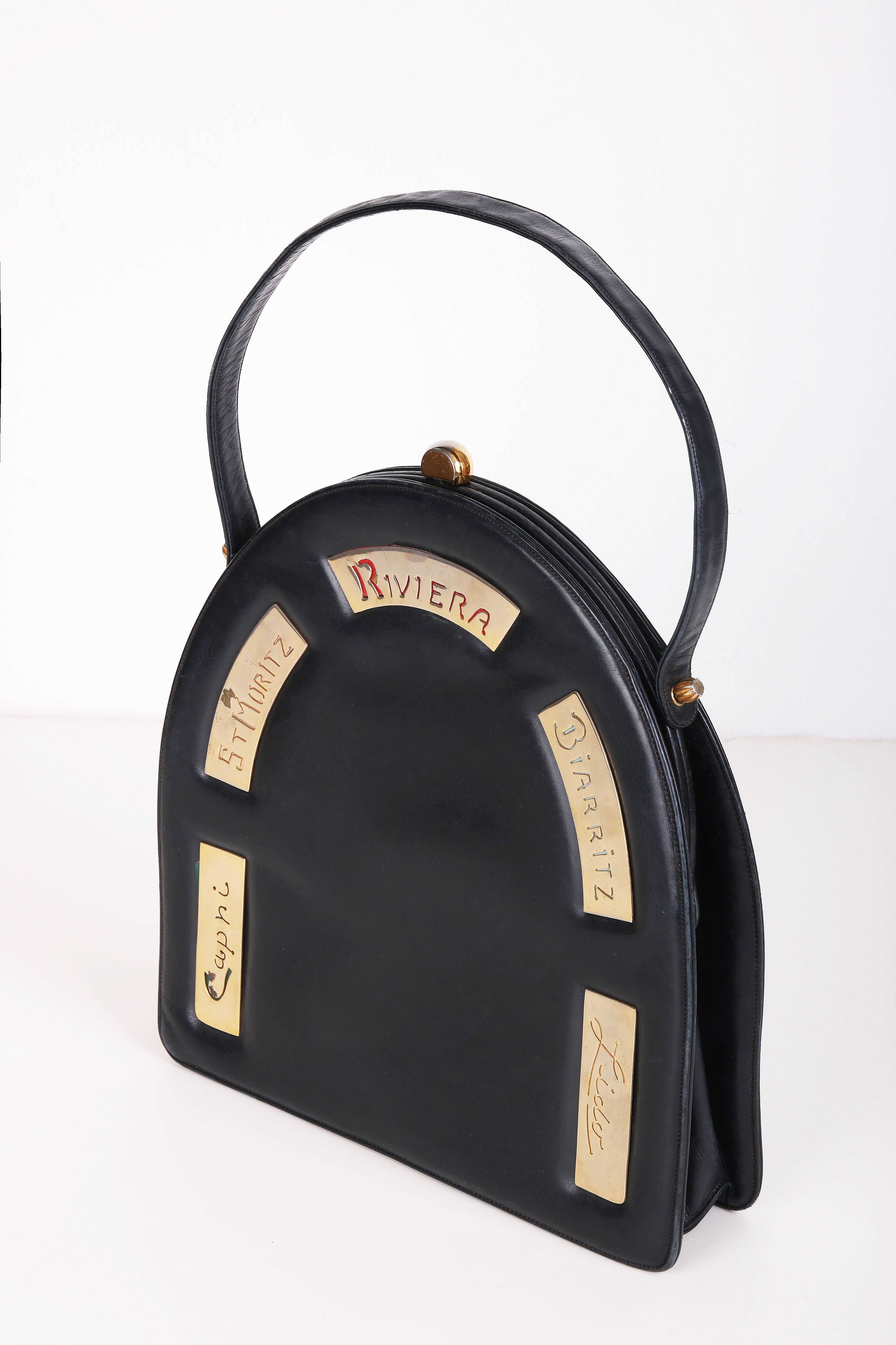 1960's Prestige black leather destination handbag in an arched shape and top handle. This bag features destination cities - Capri, St. Moritz, Riviera, Biarritz, Lido in a variety of colors on gold-toned metal plaques. Metal clasp closure. Lined in