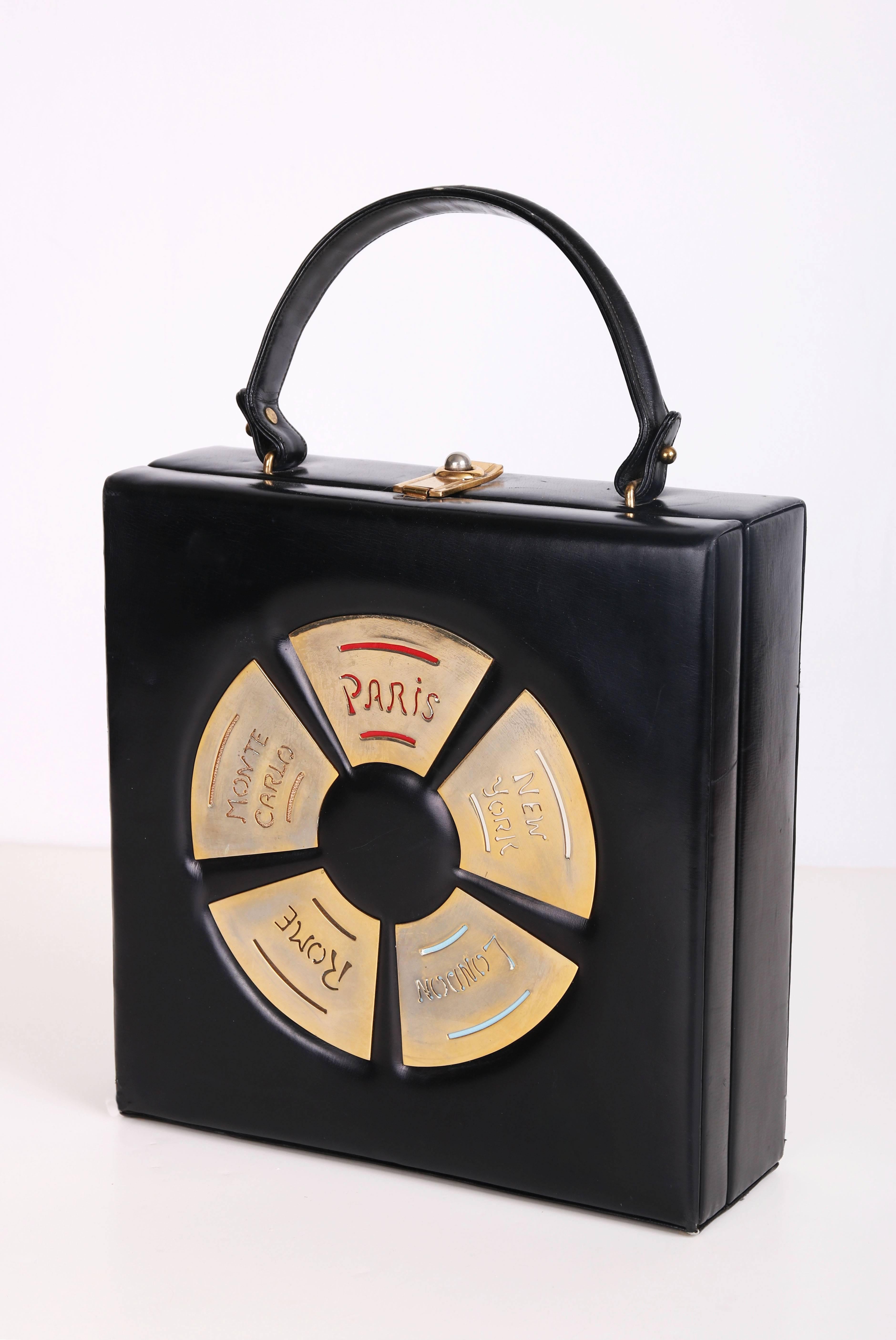 1960's Prestige black leather top-handle box handbag featuring destination city names - Paris, New York, London, Rome, and Monte Carlo in a variety of colors in gold-toned metal plaques. Metal clasp closure. Lined in a cream colored leather with