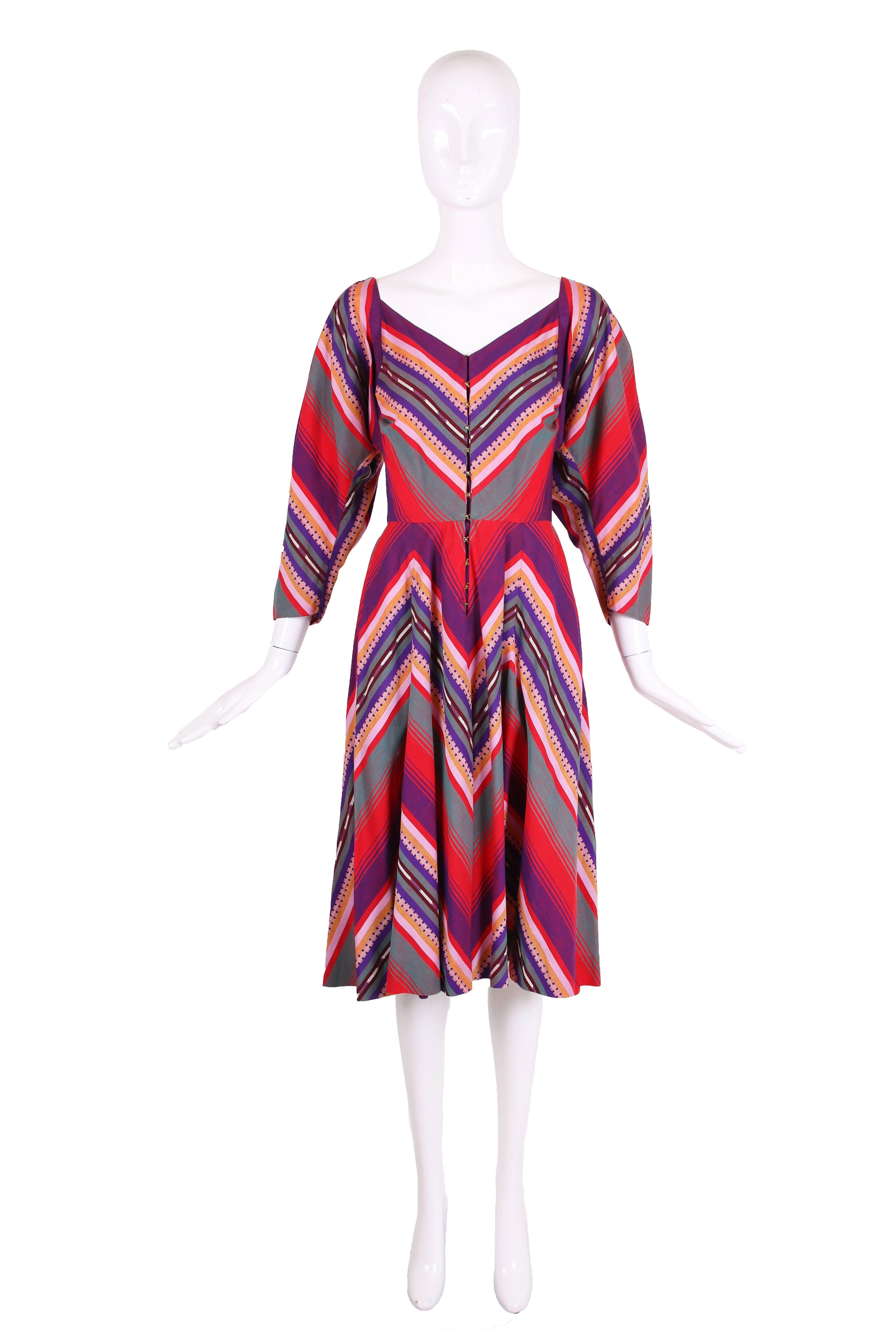 1950's Claire McCardell Clothes by Townley cotton serape print day dress in purple, red, pink, orange, navy blue, and green. Dress has a V-neck, dolman sleeves, and full skirt. Metal hook and eye closures down center front. Hidden pockets at both
