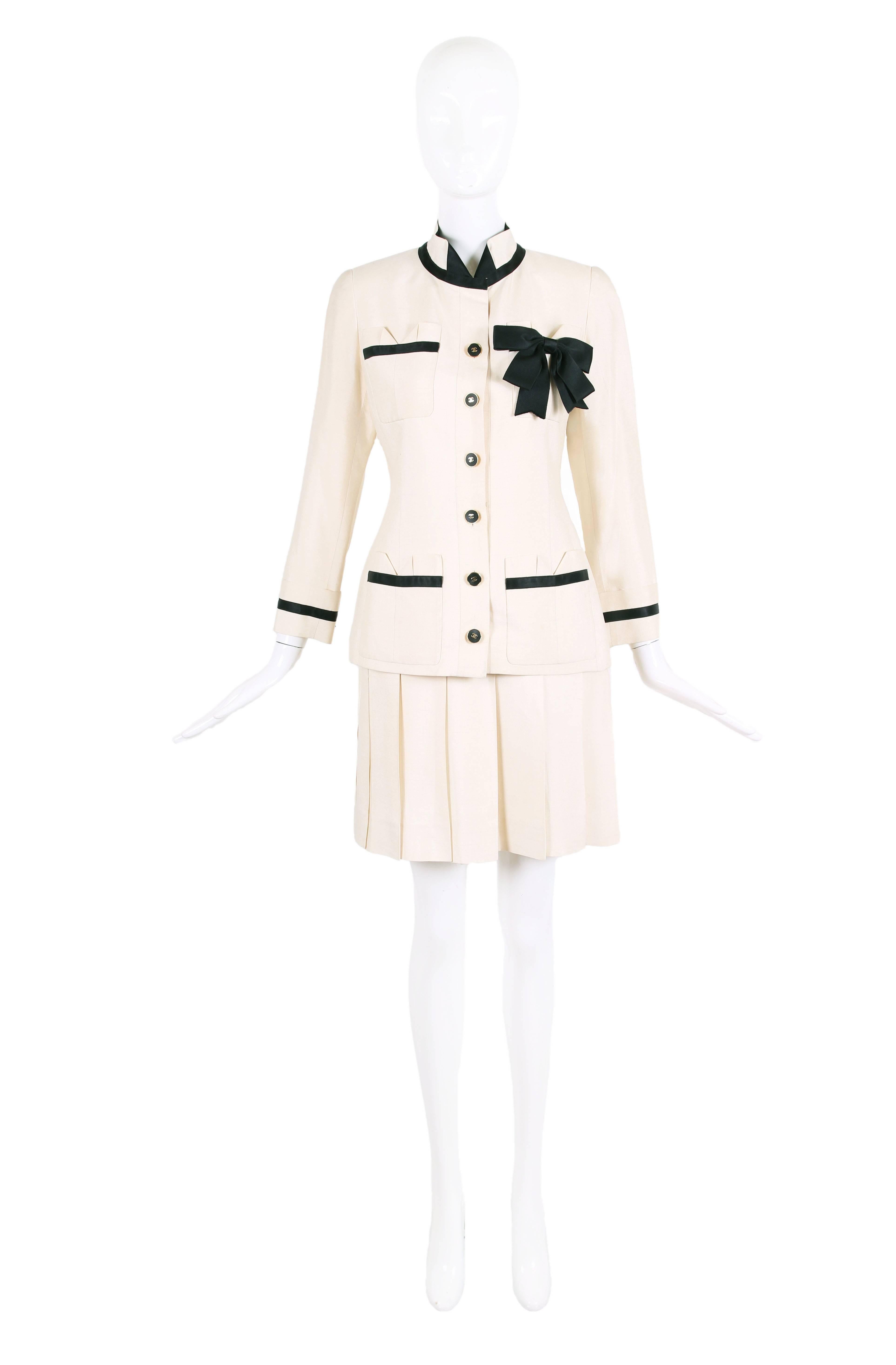 Vintage Chanel cream-colored silk shantung jacket and skirt set with black and gold CC logo button closure down center front of jacket. Jacket features a black silk band and black silk bow design motif - with black band trim at the four frontal