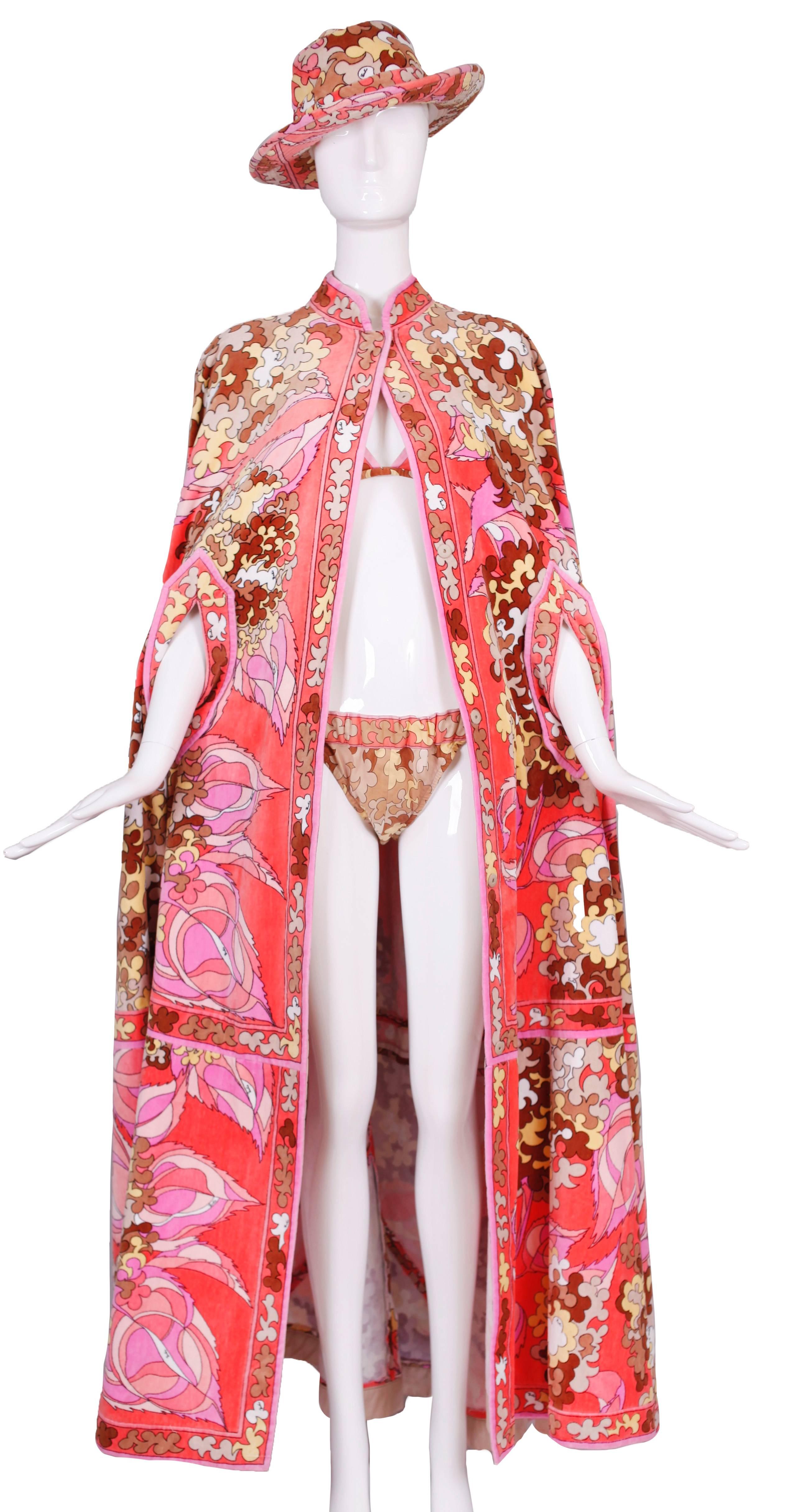 A 1960's/1970's Emilio Pucci terry cloth cape with matching terry cloth hat and cotton bikini set. The cape has a snap closure up the front and slits for arms. The bikini is cotton with a button closure at the top. The size tag for the cape is a 14