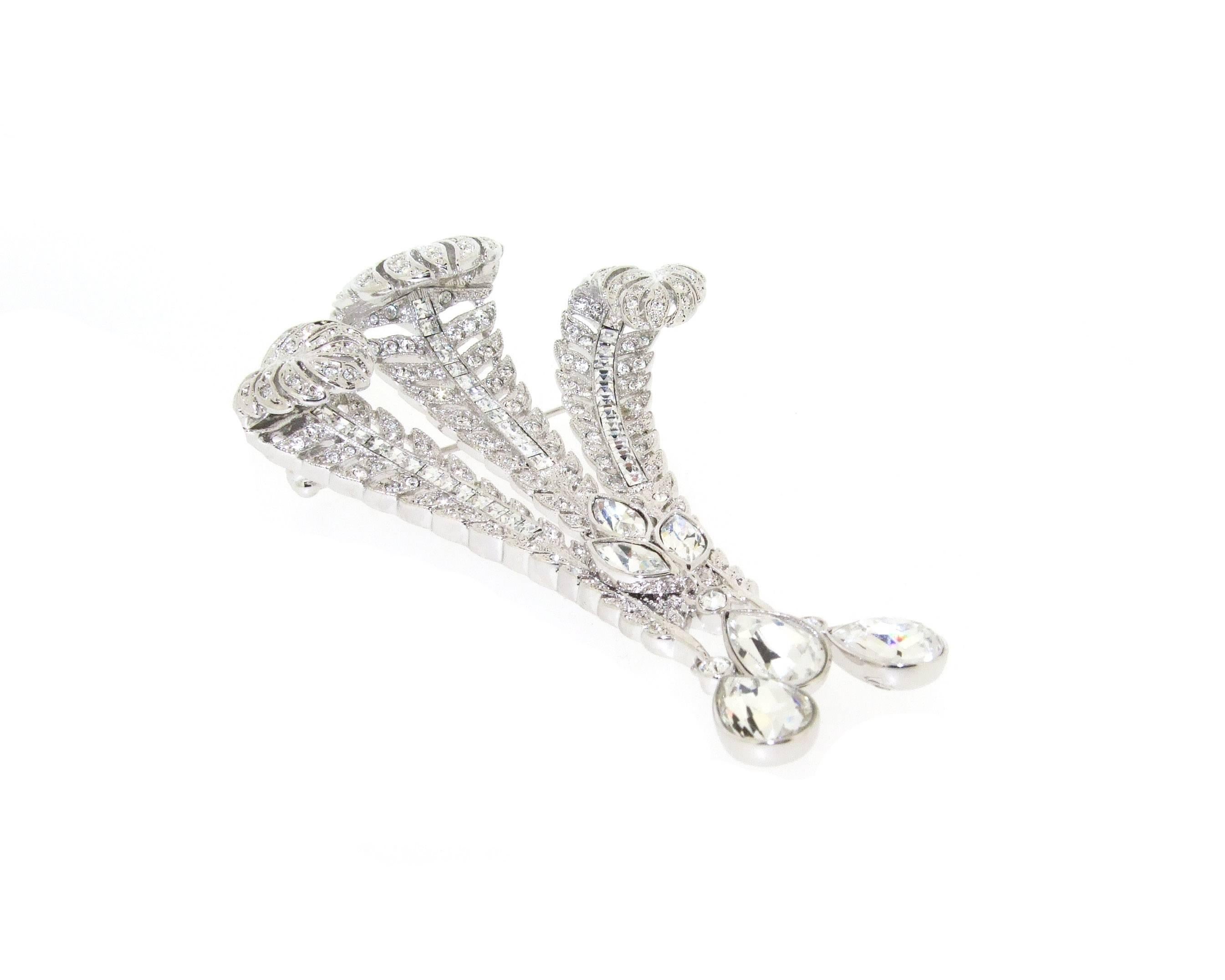 A stunning brooch depicting the Prince of Wales feathers set with cubic zirconia, with zircon triple drops.

Set in chrome plated metal, it measures 7.8cm high by 5.3cm wide at the top and 1.4cm wide at the bottom, by 1.8cm deep including the pin