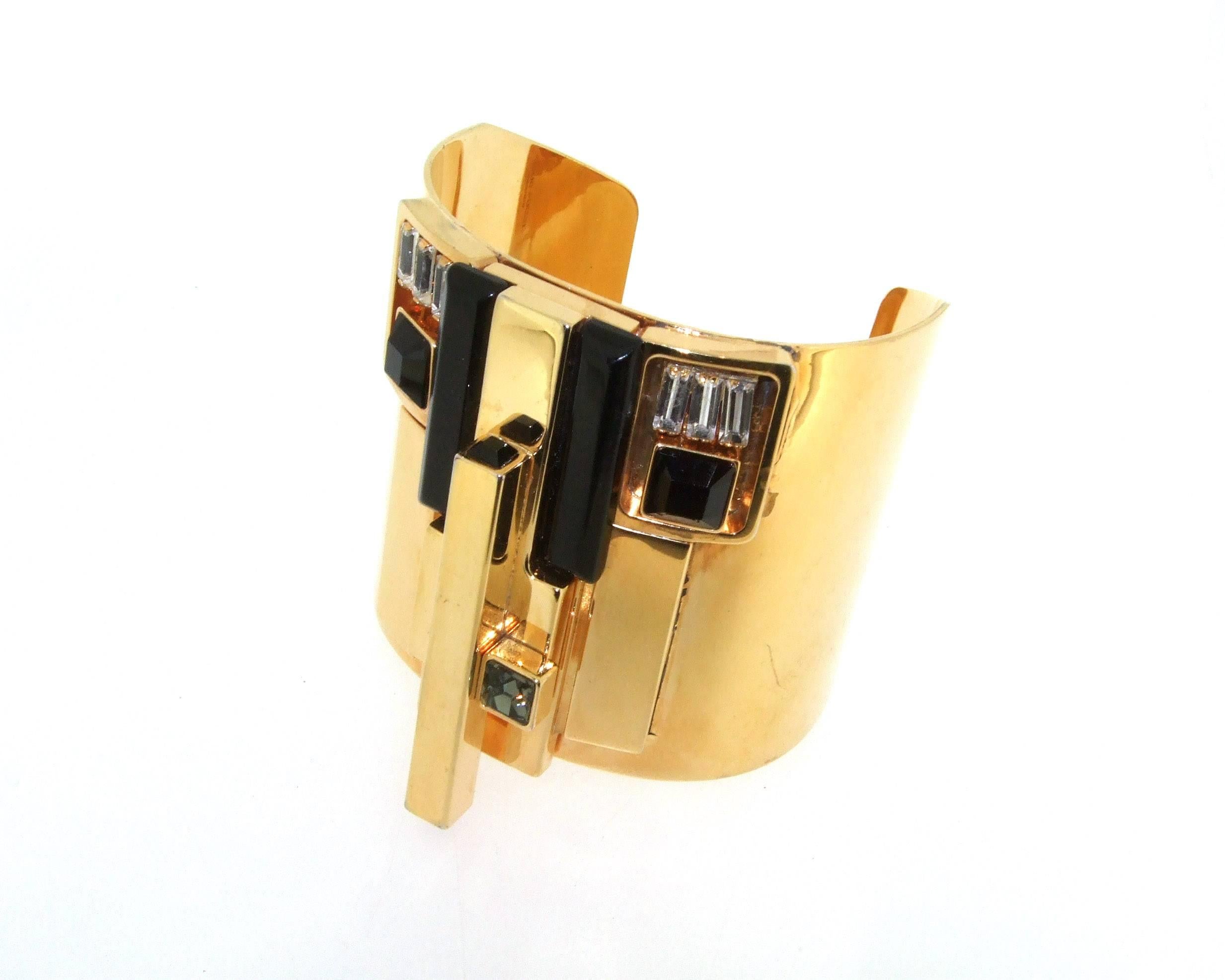 A stunning cuff bracelet by Emilio Pucci in and Art Deco stye with a modernist twist. It is made in shiny brass and set with black glass, smoky and clear crystals.

It measures 5.9cm high by 6.1cm across. 7 inches around the wrist, to fit  medium