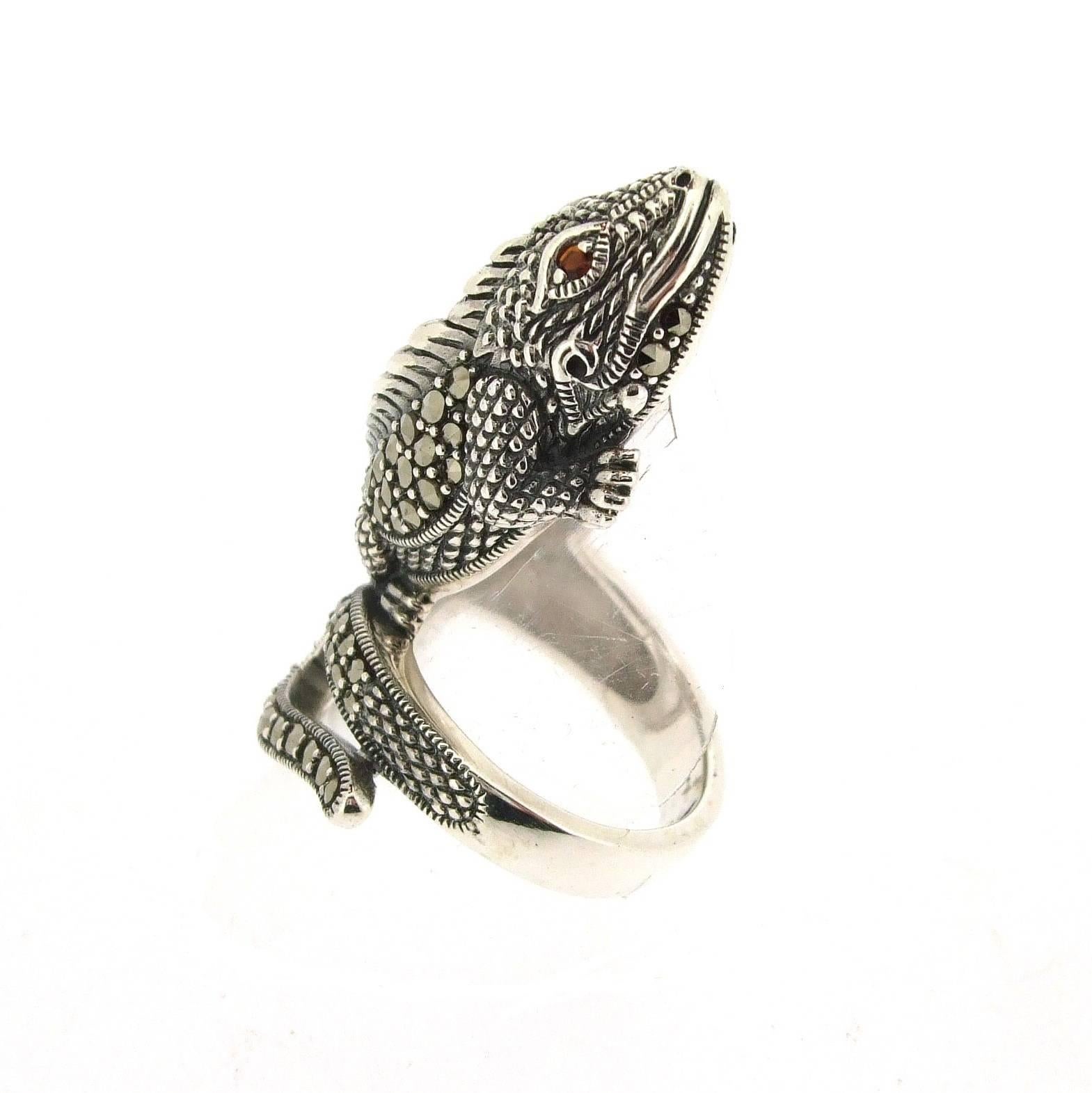 A new sterling silver ring of an Iguana/ Lizard set with sparling marcasite stones on his back and tail with garnet eyes. Silver hallmarked 925. 

