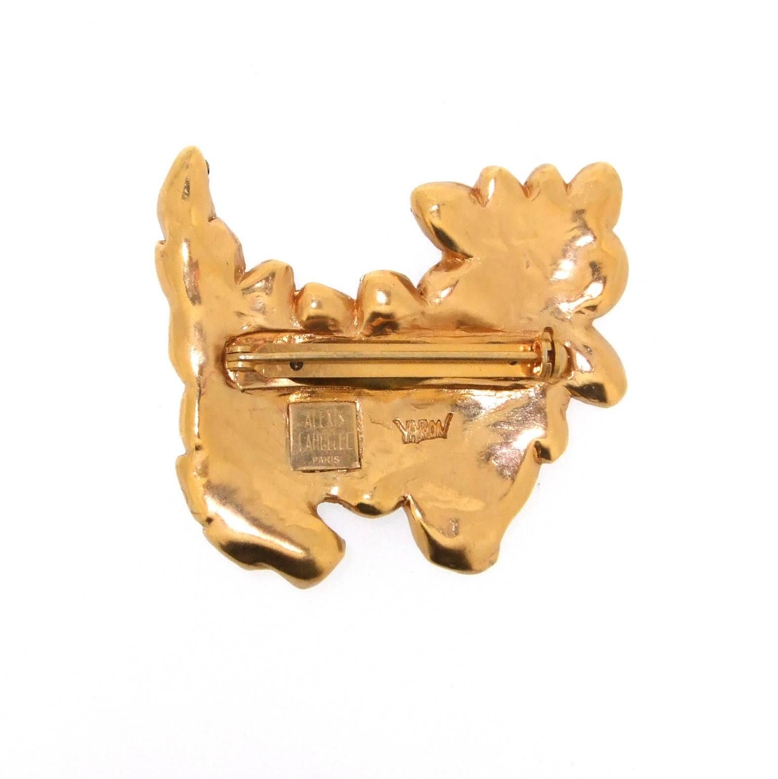 A fun abstract blue dog brooch by Alexis Lahellec in gold tone costume metal encrusted with with blue glass stones. It measures 7cm wide by 6.1cm high.