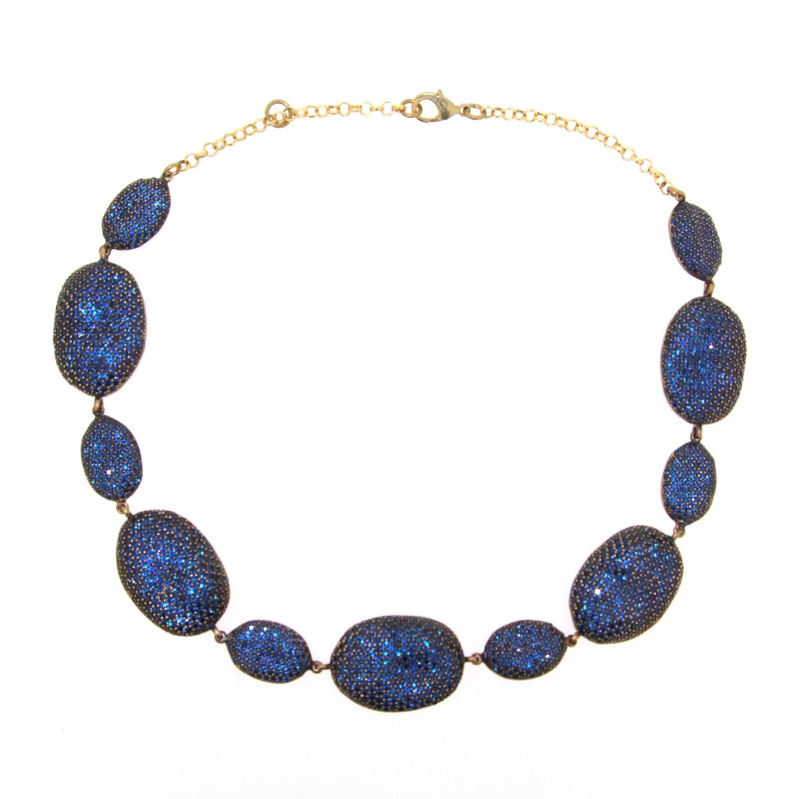 A stunning necklace by JCM London. Each pebble is encrusted with blue Iolite (a semi-precious stone in the sapphire family), they have a natural undulating uneven formation to give it the feel of the shape of a natural pebble. 

The smaller ovals