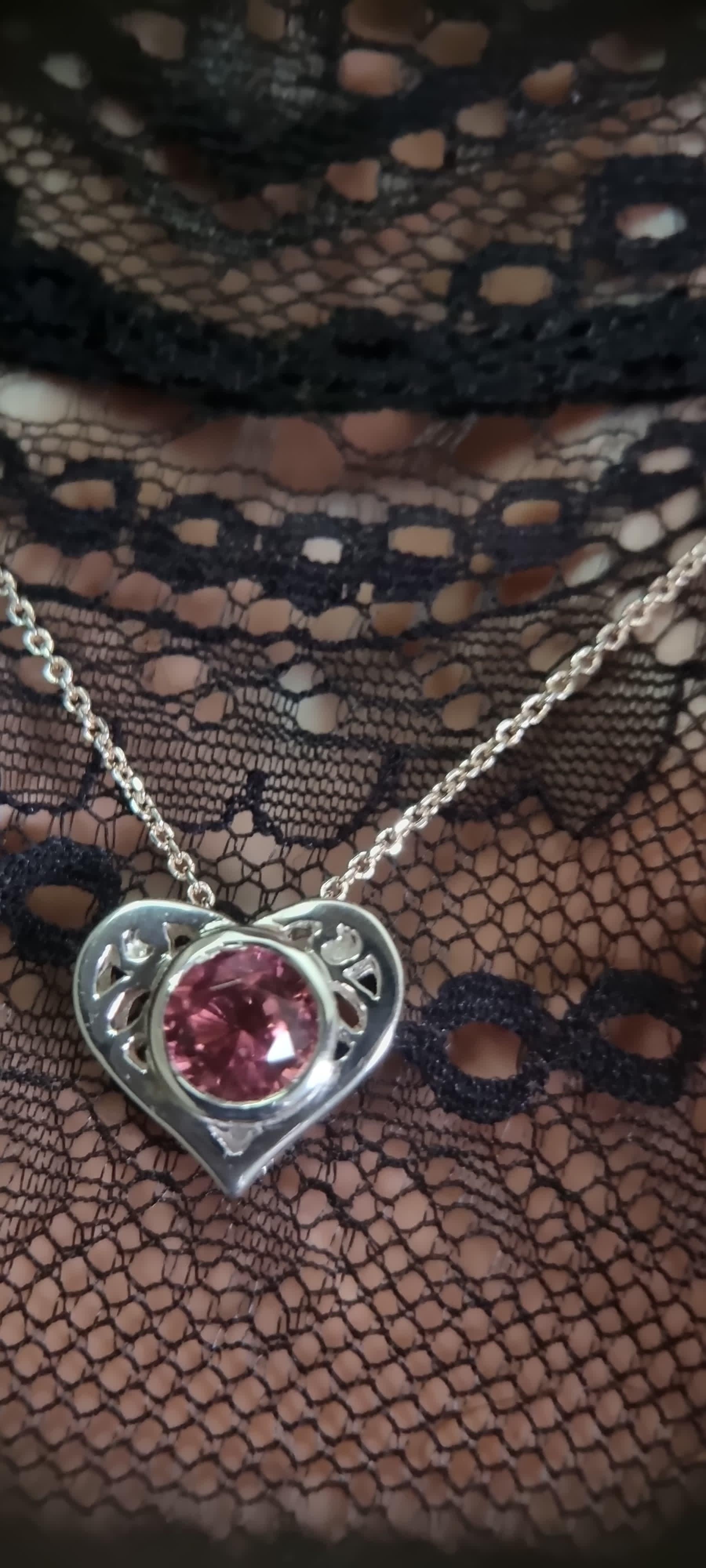 This necklace pendant features a 9.6 x 9.1mm round natural pink tourmaline, notable for its vibrant blush hue and high clarity. The gemstone is securely housed within a heart-shaped sterling silver setting, weighing 9 grams. The sterling silver