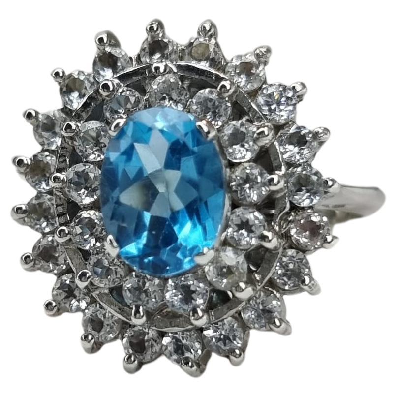 Indulge in the captivating allure of our 1-carat Oval Natural Blue Topaz Cocktail Ring. This exquisite piece marries the purity of simplicity with the brilliance of a genuine blue topaz encircled by Natural Sparkling Zircon, resulting in a timeless