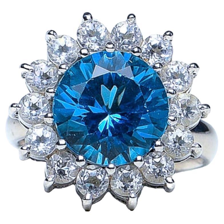 The Natural 5ct Round Natural Blue Topaz Cocktail Ring. This exquisite piece marries the purity of simplicity of white Zircons with the brilliance of a genuine blue topaz, resulting in a timeless and sophisticated accessory.

Product