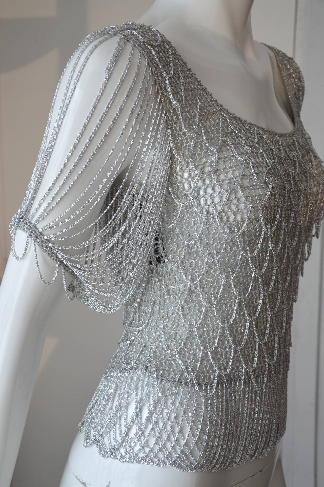 1970s Loris Azzaro top silver crochet knit in metallic silver thread. The bottom of the top has a fringe made with silver chain. The same chain is used over the sweater, the dramatic sleeves feature the same chain mail detail.
Sophisticated top and