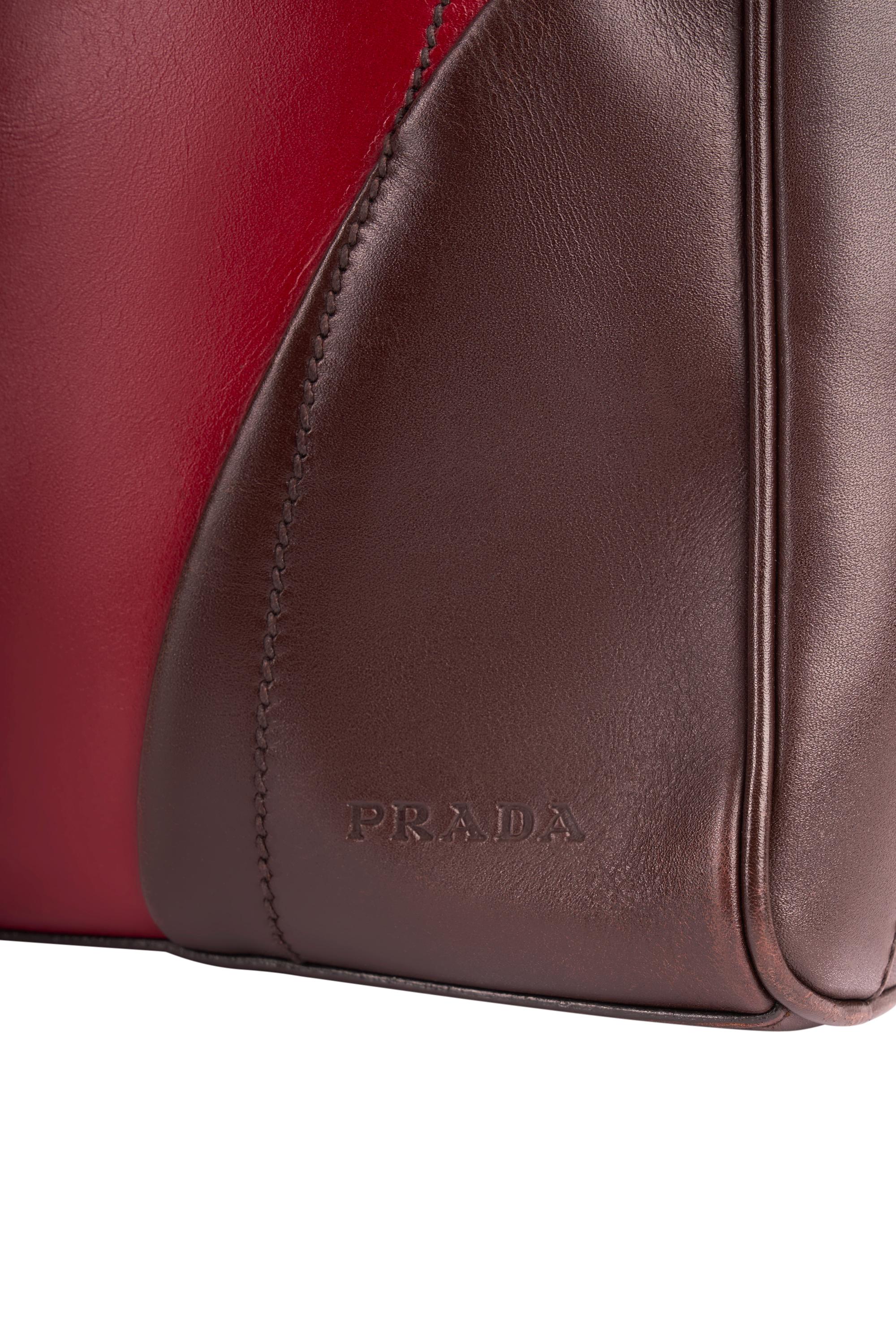 Sac en cuir rouge et marron Prada 1990. Il est doté d'une poignée supérieure, de couleurs bicolores marron et rouge, d'accessoires Prada et d'un logo gravé sur le devant en bas à gauche. Fermeture à glissière sur le dessus et fermeture à glissière à