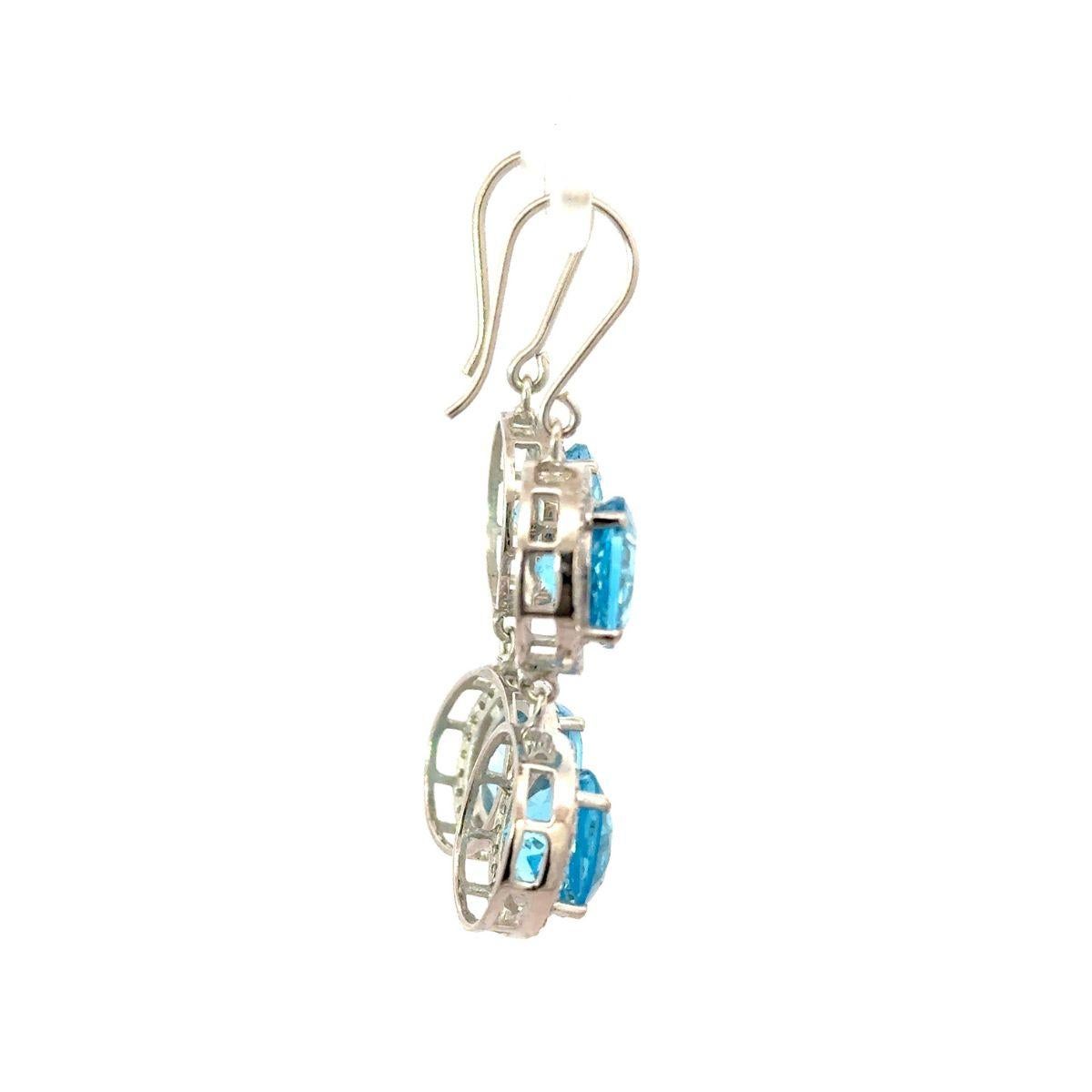 Questi orecchini a goccia in argento con zircone con doppio alone di topazio blu sono caratterizzati da due vibranti gemme di topazio blu dal taglio rotondo, ciascuna circondata da un alone di pietre bianche scintillanti, incastonate nel luminoso