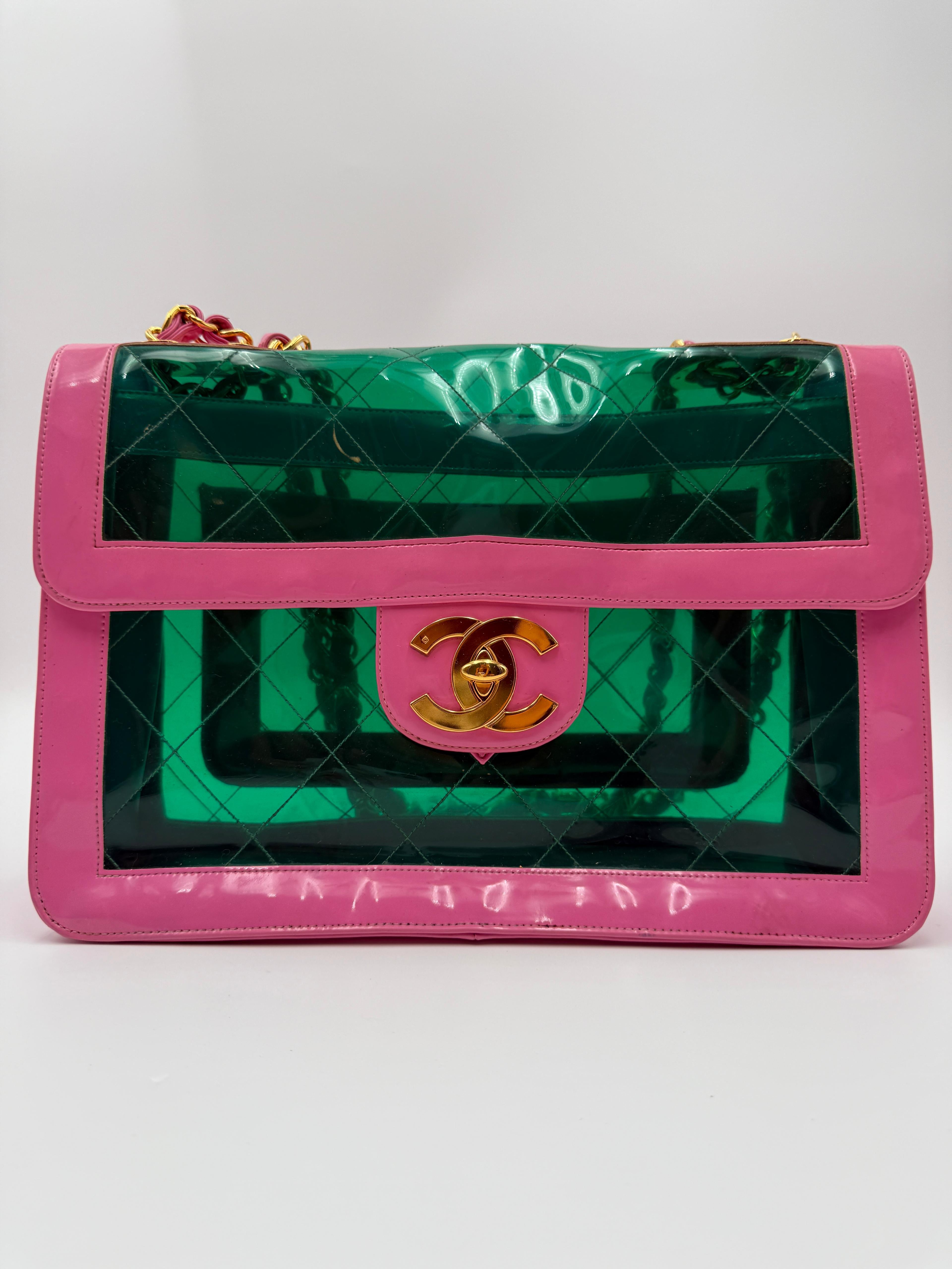 Questa rarissima maxi borsa con patta di Chanel del 1995 è caratterizzata da un iconico corpo in PVC verde smeraldo traslucido, con finiture in pelle rosa e un sorprendente logo CC in oro sul davanti. Un vero e proprio pezzo da collezione dell'epoca