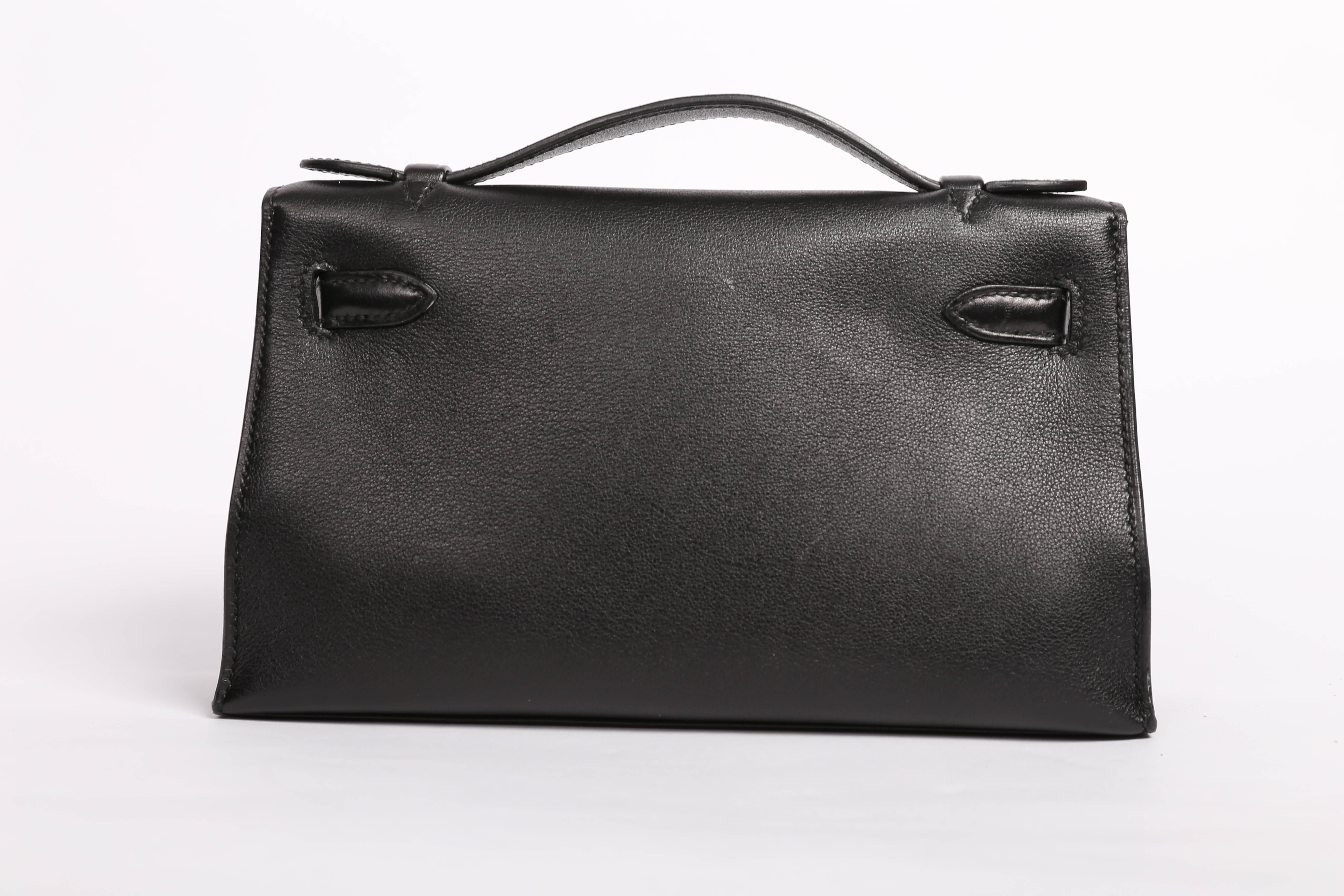 Hermes  Kelly Pochette in black swift leather with palladium hardware.

Kelly Pochette features tonal stitching, a front flap with two straps, toggle closure and single flat handle. The interior is lined in black chevre and with one flat interior