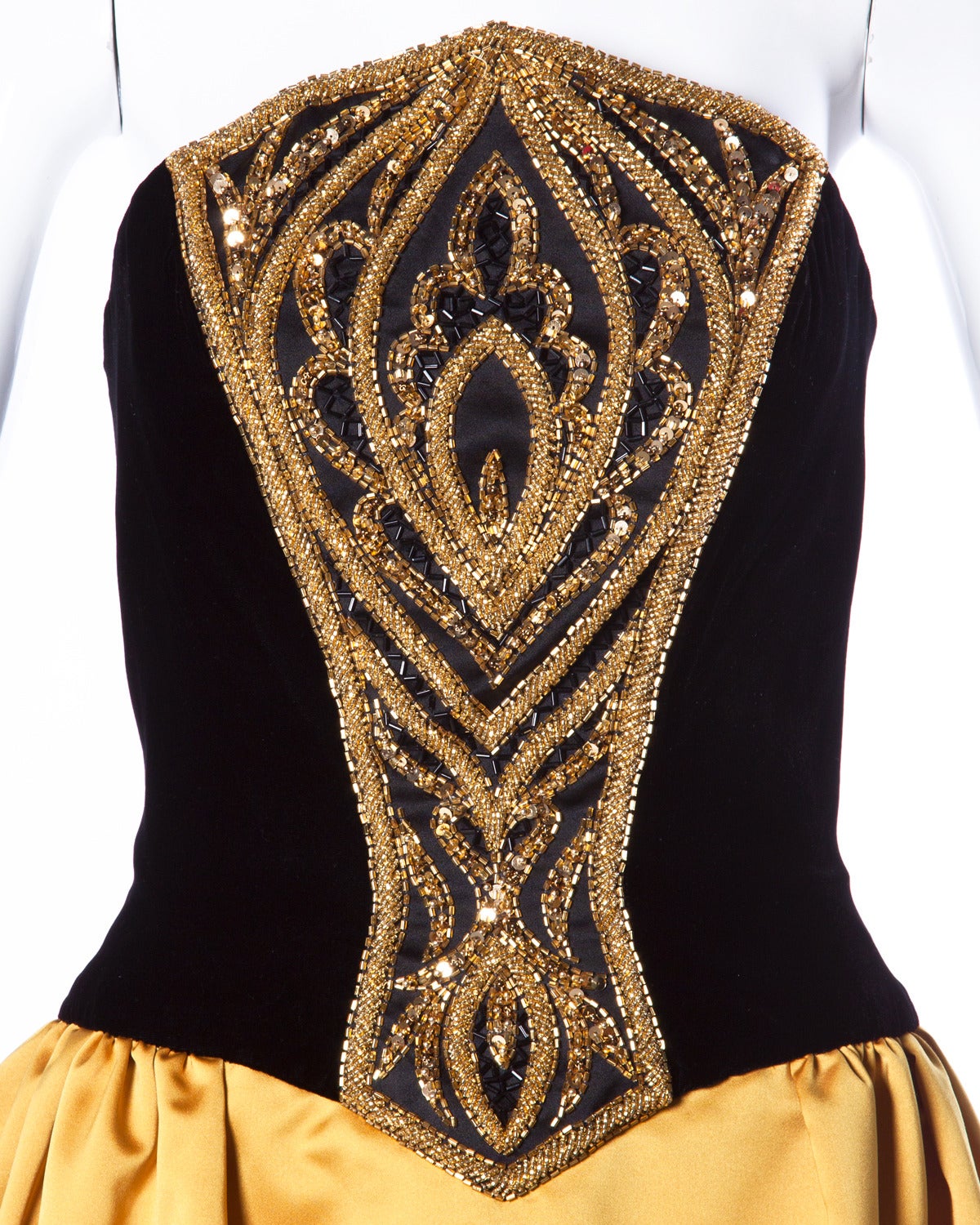 Strapless Bob Mackie evening dress with a velvet bodice and gold satin skirt. Heavy glass beaded embroidery down the front of the dress.

Details:

Fully Lined
Back Zip and Hook Closure
Marked Size: 8
Color: Black/ Gold/ Gold Iridescent/