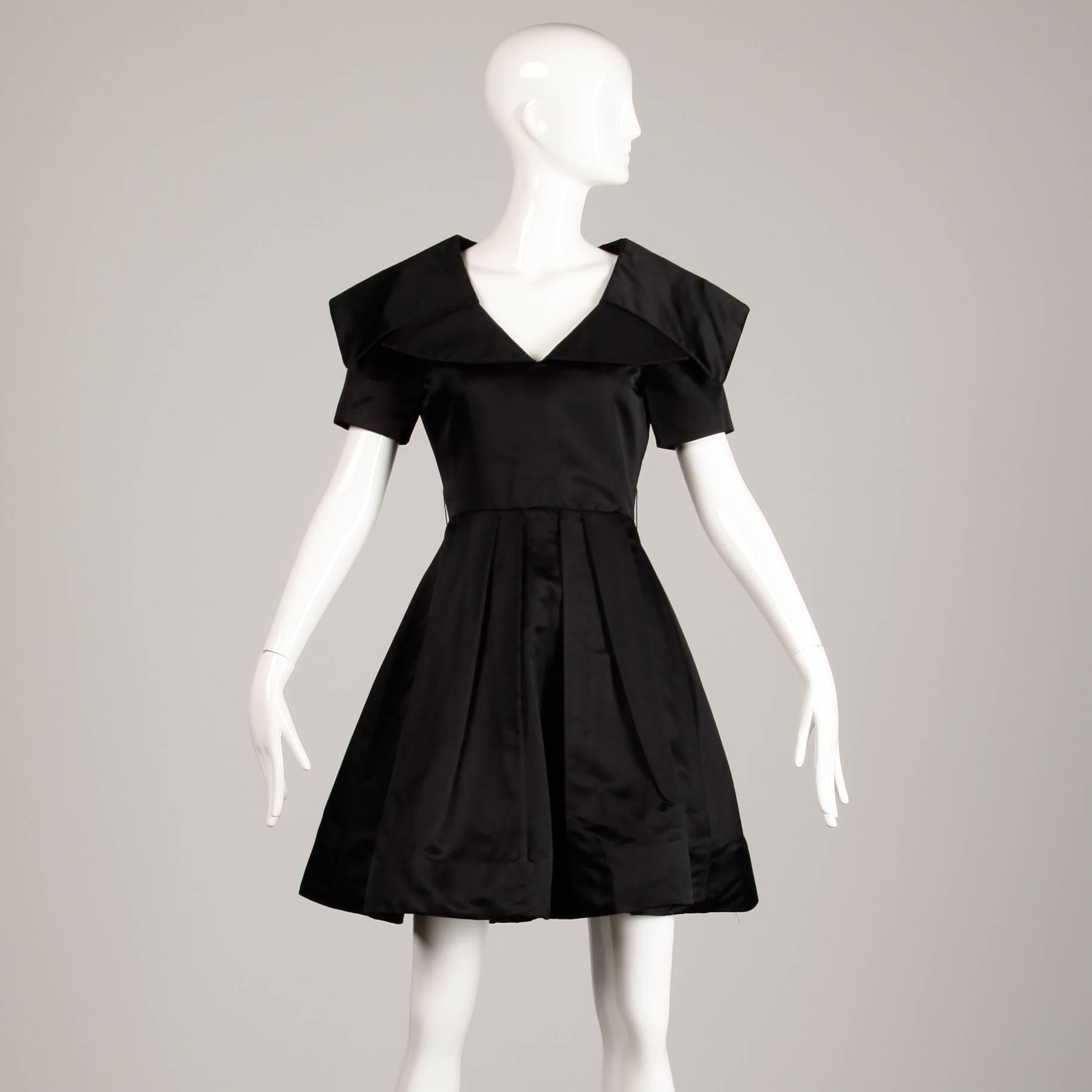 Gorgeous heavy weight black silk satin dress by Arnold Scaasi. Oversized collar and pleated skirt. Fully lined in silk with rear zip closure. The dress fits like a modern size small-medium. The bust measures 35", waist 27.5", shoulders