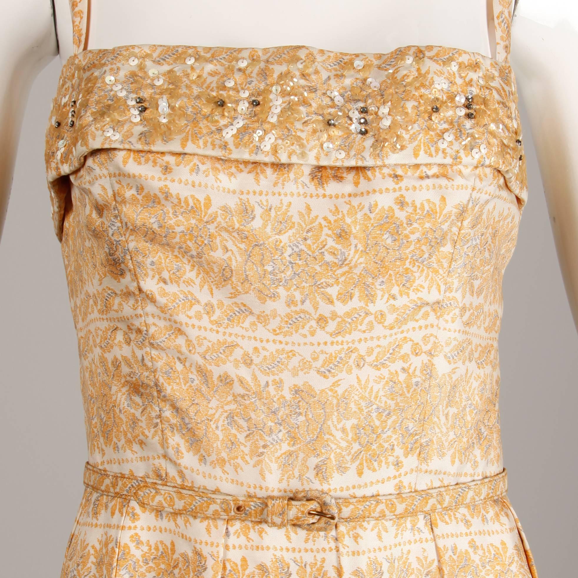 Stunning vintage 1950s silk dress in a mustard yellow floral print by Anna Miller. Sequin, bead, and rhinestone detail across the bust and matching leather backed belt. Box pleats and covered buttons up the back. Partially lined with rear metal zip