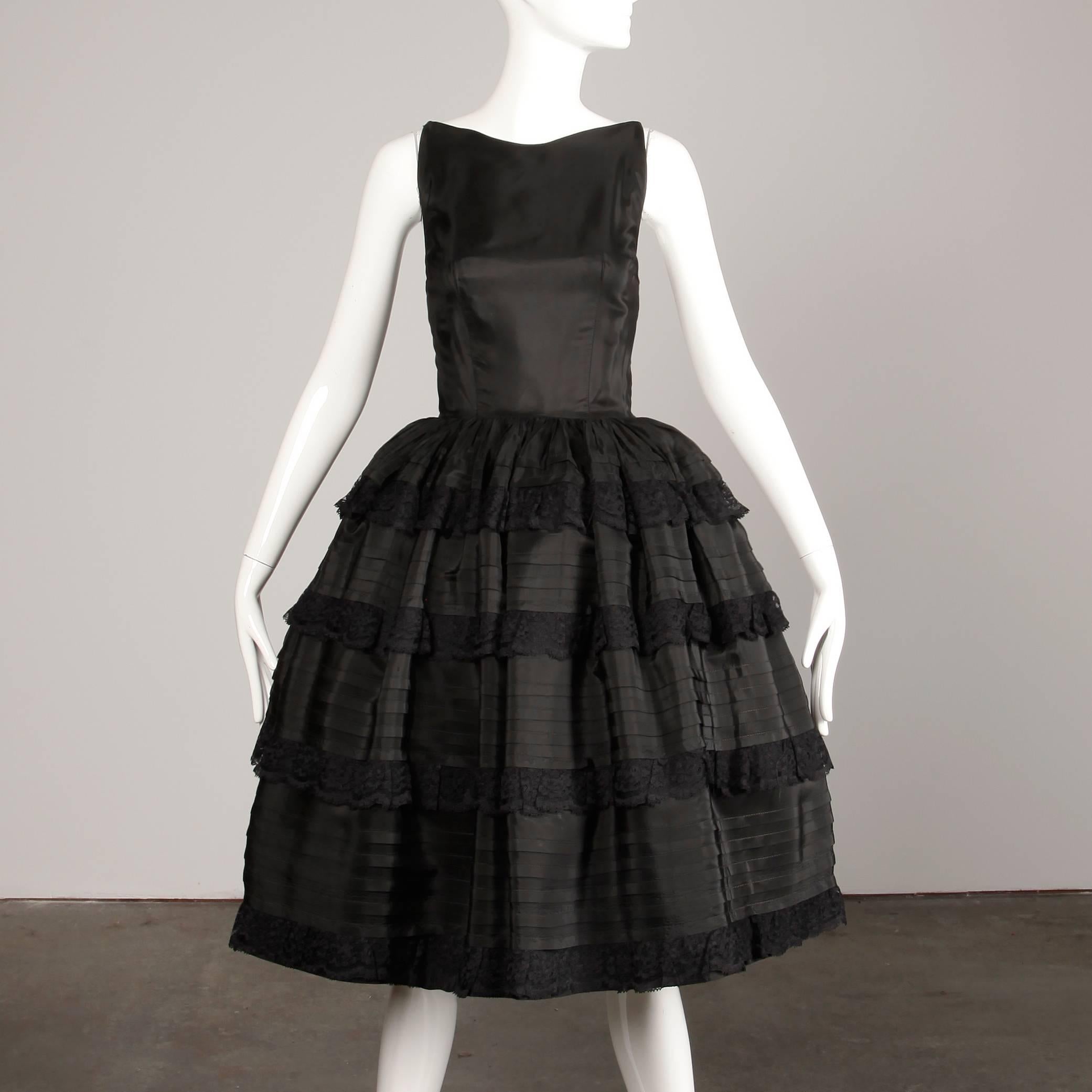 Elegant 1950s vintage black taffeta and lace cocktail dress with a scoop back and full tiered skirt. Partially lined with rear metal zip and hook closure. Fits like a modern size small. The bust measures 40", waist 26", hips free, and the
