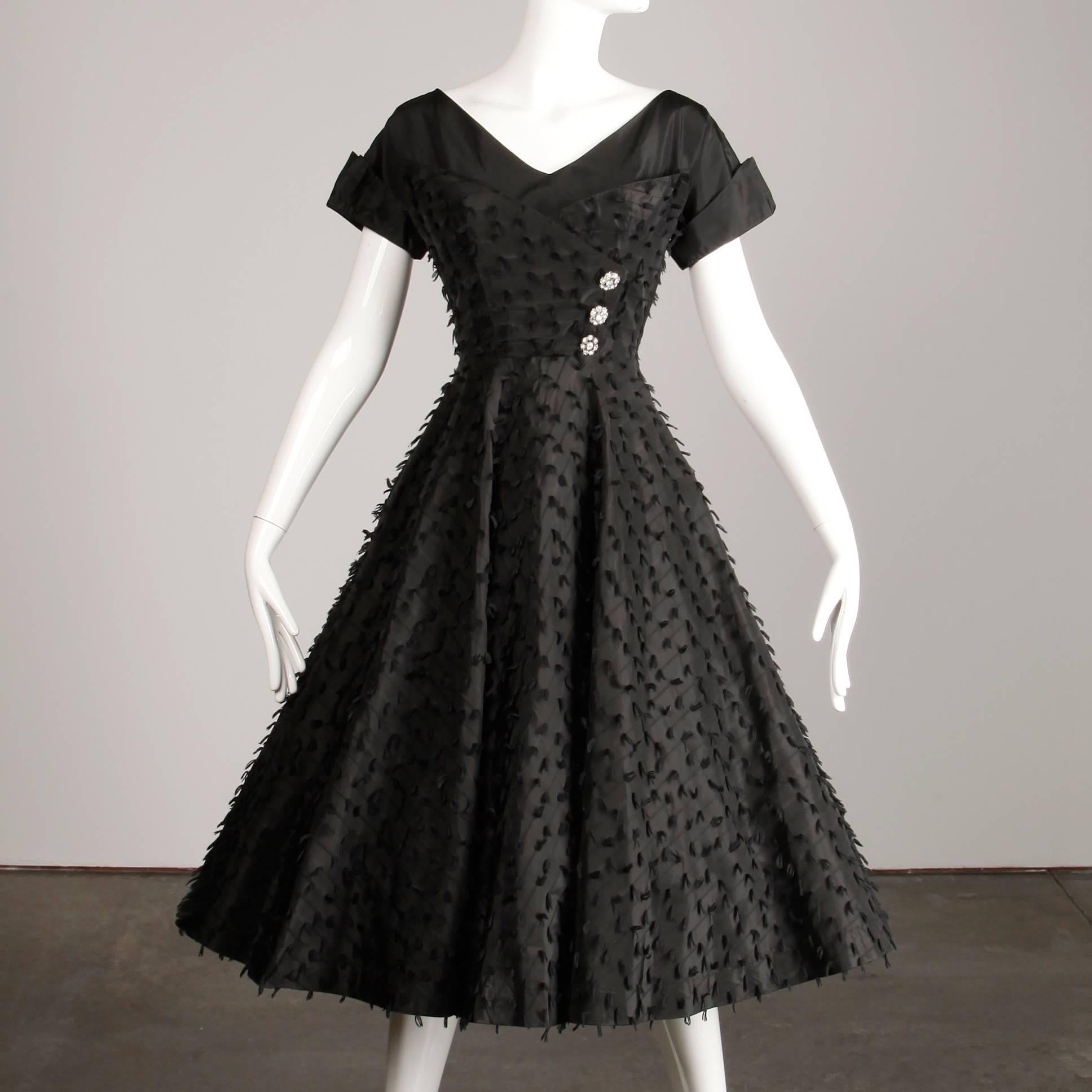 Gorgeous vintage 1950s cocktail dress in a black eyelash taffeta. Features a full sweep and three asymmetric rhinestone buttons. Unlined with side metal zip closure. Fits like a modern size S-M. The bust measures 37