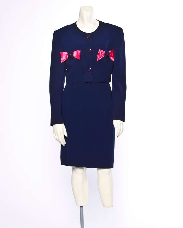 Adorable navy blue cropped jacket and pencil skirt suit with bright pink satin bows by Valentino Night. Both pieces are fully lined and perfectly tailored. The jacket features shoulder pads and buttons up the front. The skirt has rear zip and hook