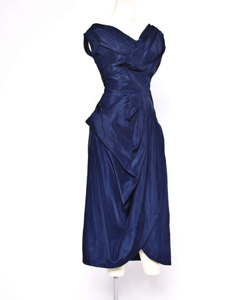 Gorgeous 1950s midnight blue draped silk cocktail dress with a nipped waist and metal side zipper. Unlined with side zip and hook closure.

This is an estimated size small with the following measurements:

Bust: 36