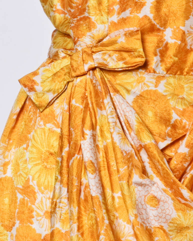 Floral print silk cocktail dress with short sleeves and draped bow detail on the front.

Details:

Fully lined
Back metal zip and button closure
Circa: 1960's
Estimated size: M
Color: White/Yellow/Orange
Fabric: Silk

Measurements: