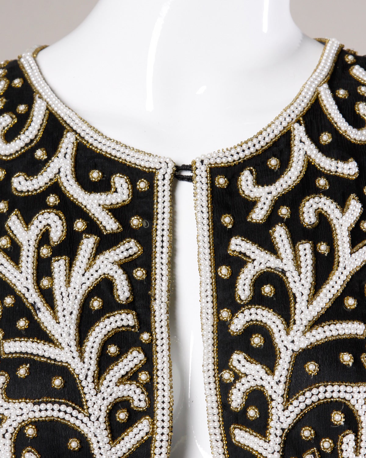 Heavily beaded silk jacket with a pearl and seed beaded design.

Details:

Fully Lined
Front Hook Closure
Marked Size: Not Marked
Estimated Size: Medium
Color: Black/ White Iridescent/ Gold Iridescent
Fabric: 100% Silk/ Rayon