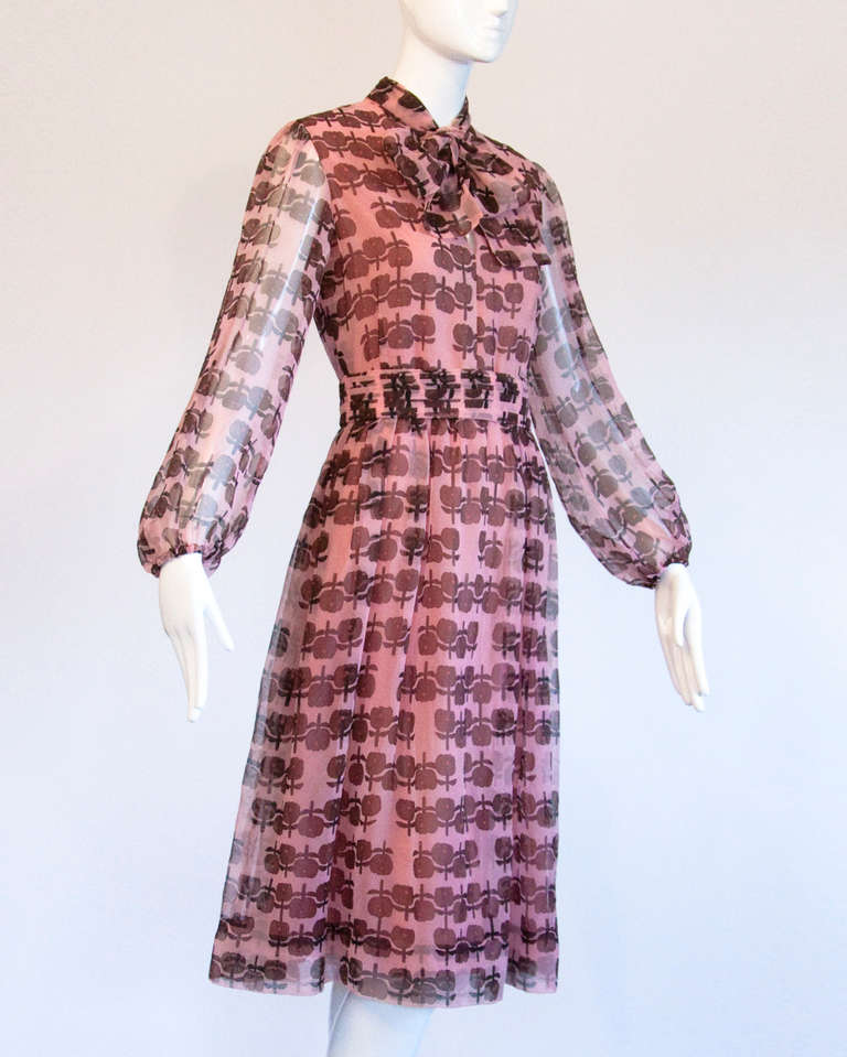 Darling dusty pink and plum floral printed dress with an attached ascot bow tie. By Helga. Partially lined with sheer sleeves. Rear zip closure.

This dress will best fit a modern size 2-4 small.

Shoulders: 15