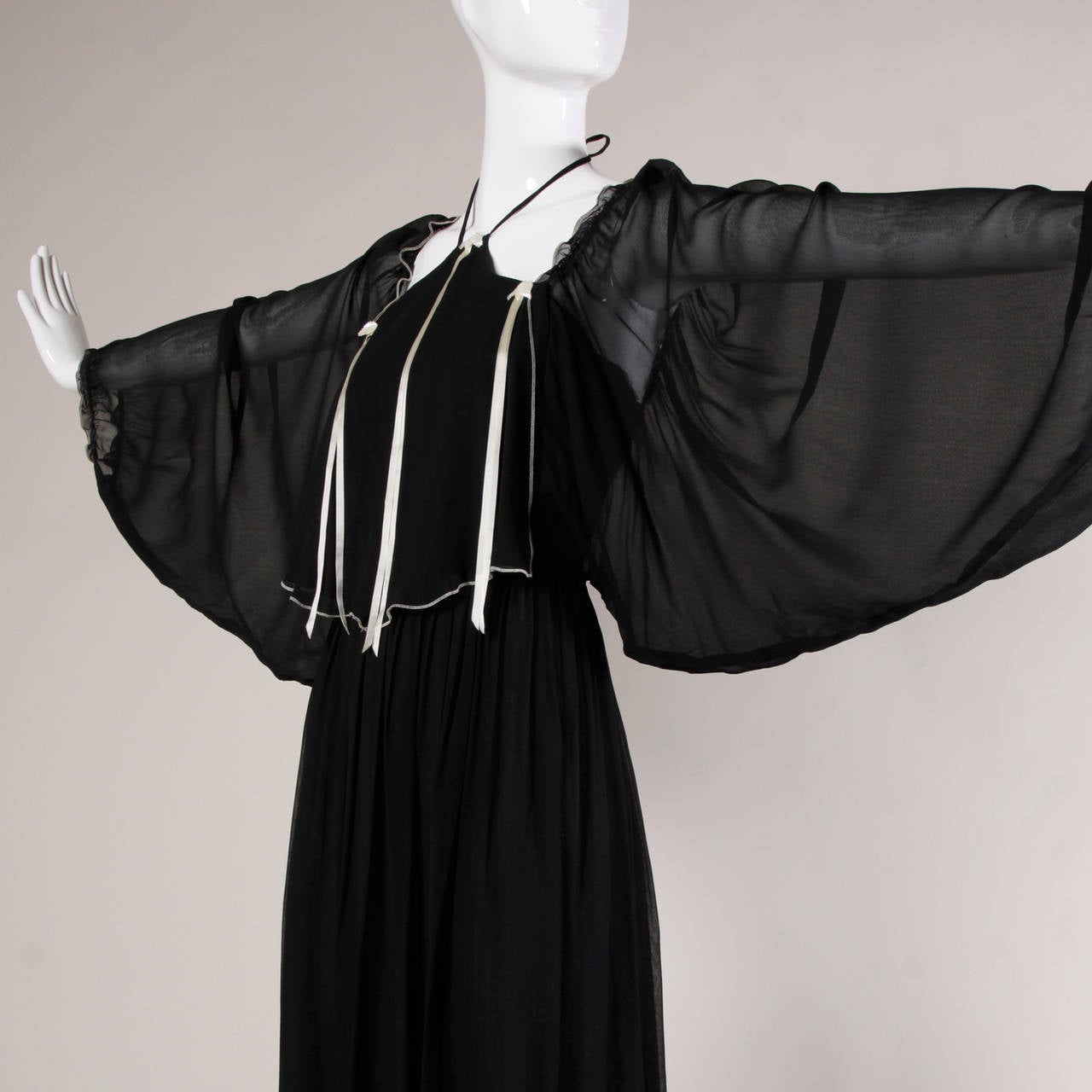 Unique 1970s black maxi dress with bat wing sleeves and a halter neckline.

Details:

Fully Lined
Back Zip and Hook Closure/ Ties At Neck
Marked Size: Not Marked
Estimated Size: Medium
Color: Black/ Pale Beige Ivory/ Iridescent Ivory, Pastel