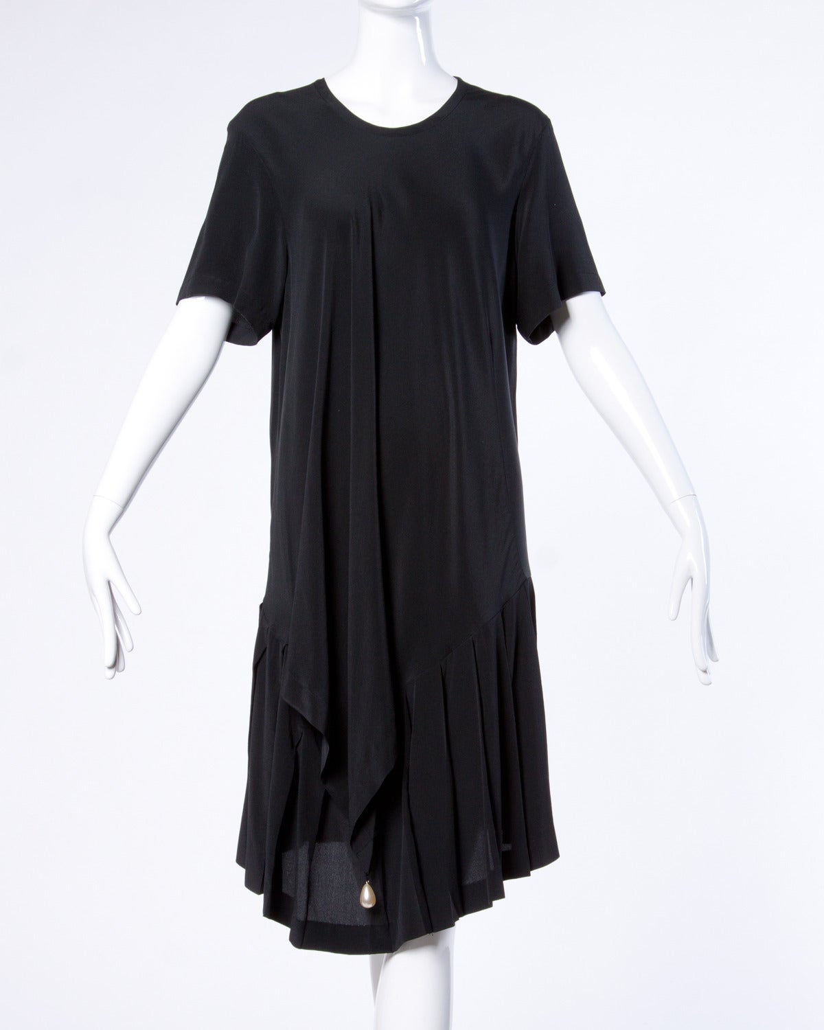 Avant garde black silk midi dress by Comme des Garcons. Asymmetric detail near the bottom of the dress where there is a pearl weight that can be tucked inside or worn outside the dress. Short sleeves and rounded