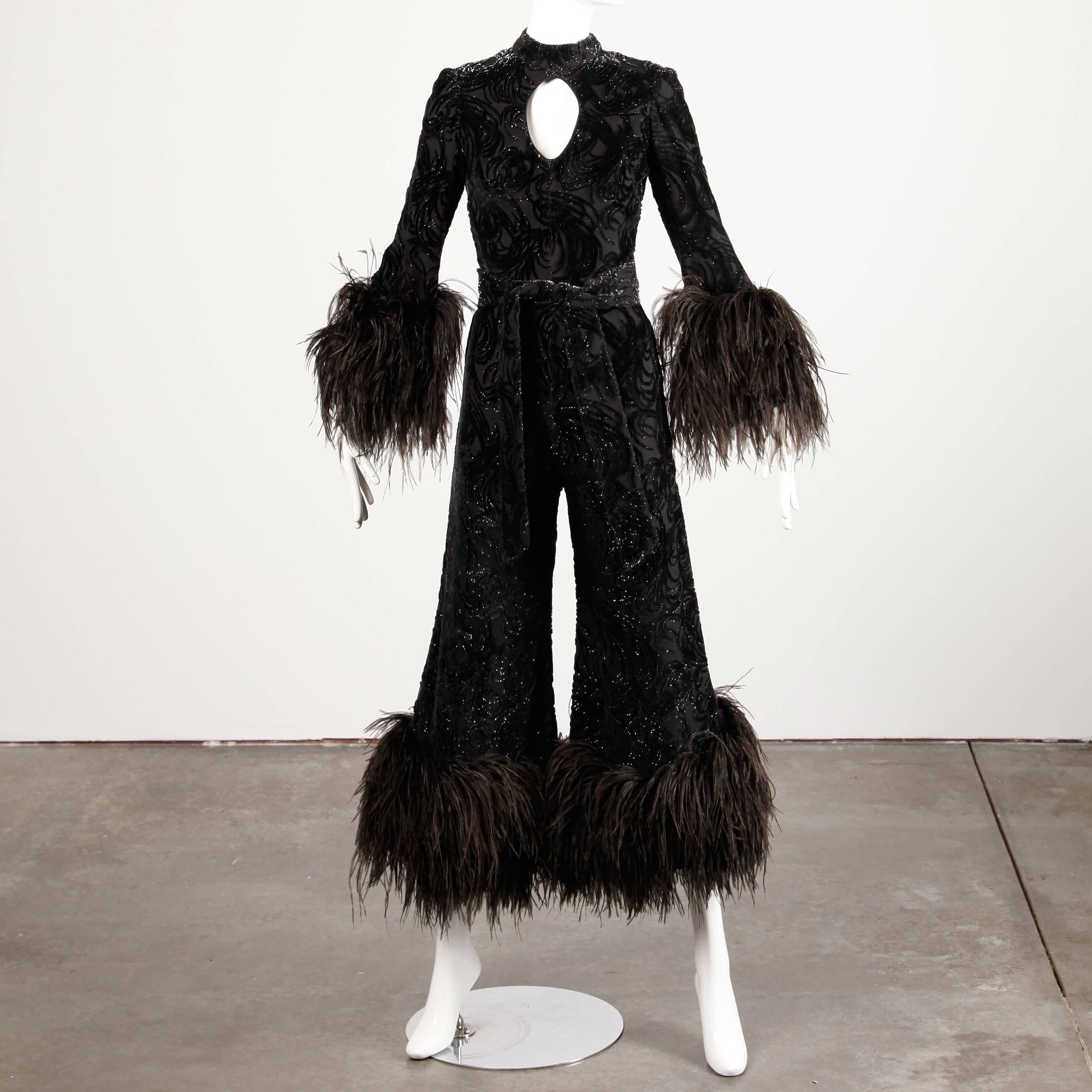Show stopping vintage 1970s black burnout velvet jumpsuit with massive ostrich feather cuffs and a cut out keyhole neckline by Lillie Rubin. Fabric is textured with flecks of metallic. There is a matching sash that ties around the waist and is not