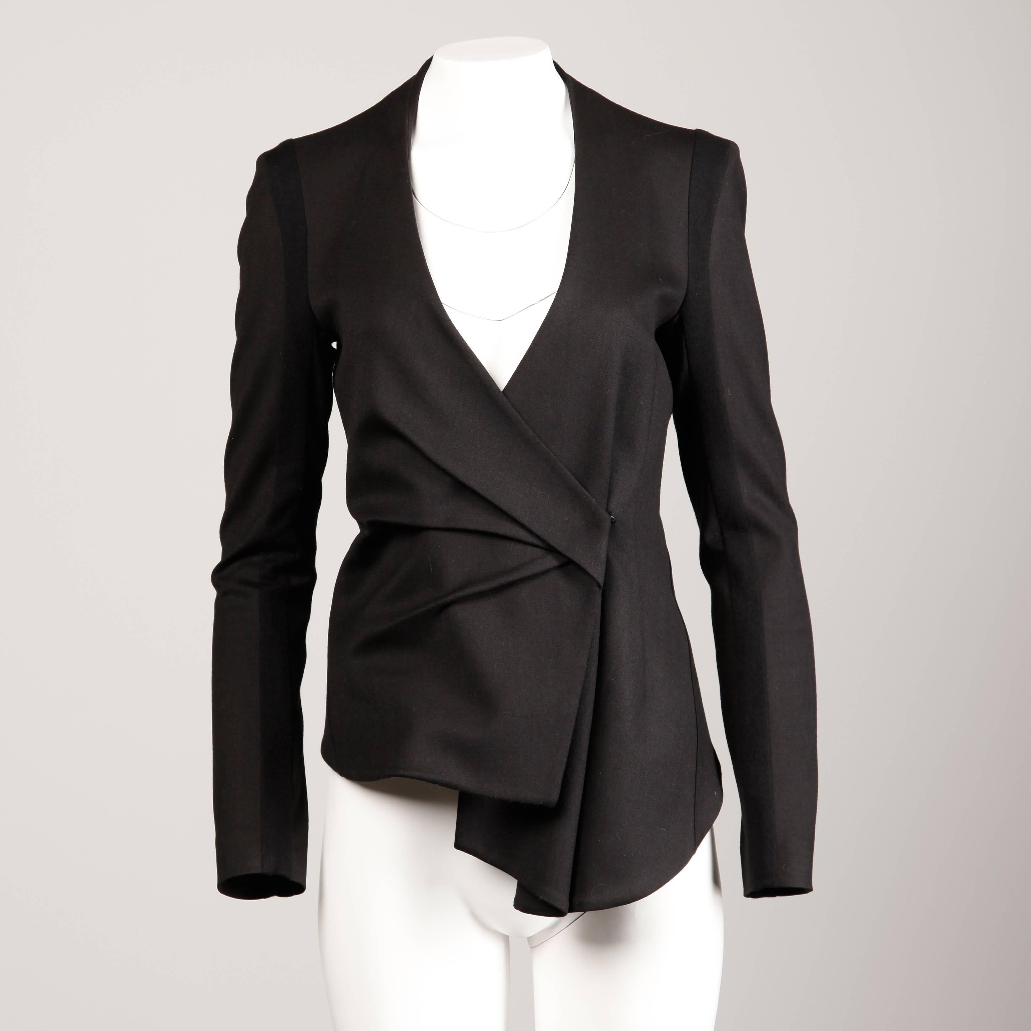 Chic black wool asymmetric blazer jacket by Helmut Lang with bold shoulders and hook closure. Fully lined in 95% silk 5% spandex fabric. The fabric content is 97% wool 3% lycra. The marked size is 2 and the jacket fits true to size. The bust