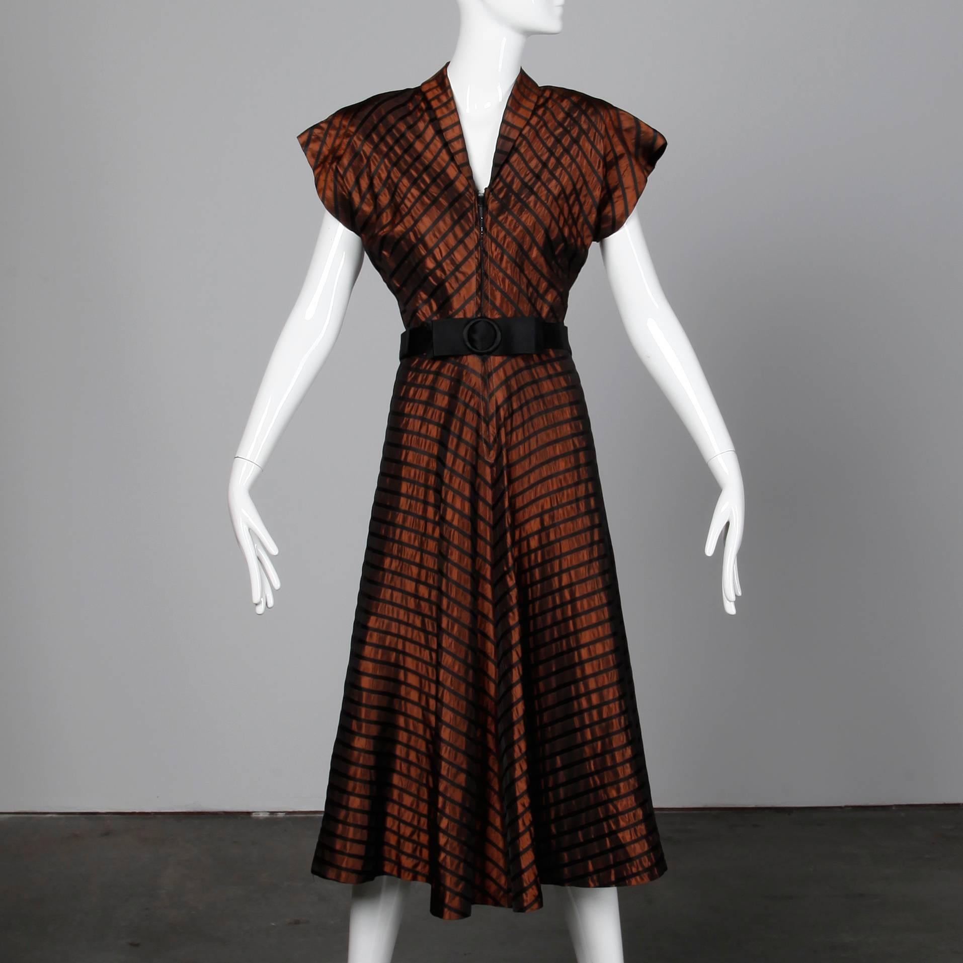 Classic 1940s vintage dress in brown and black taffeta. Unlined with front metal zip closure. The bust measures up to 36", waist 27", hips up to 44", and the total length 49". The belt measures 35" long and 1.5" wide.