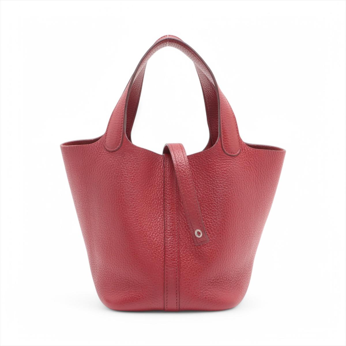 Le Picotin Lock 18 PM en cuir Taurillon Clémence, présenté dans la teinte Rouge Garance, incarne un mélange d'élégance intemporelle et de design pratique. Fabriqué en cuir Clémence souple et durable, le sac présente une texture grainée qui ajoute à