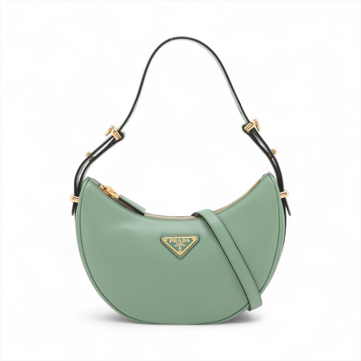 La borsa a tracolla a due vie in pelle di Prada Arque in colore verde Sage è un accessorio di ottima fattura caratterizzato dalla caratteristica forma a mezzaluna che aggiunge un tocco di moderna eleganza a qualsiasi outfit. Il suo design elegante e