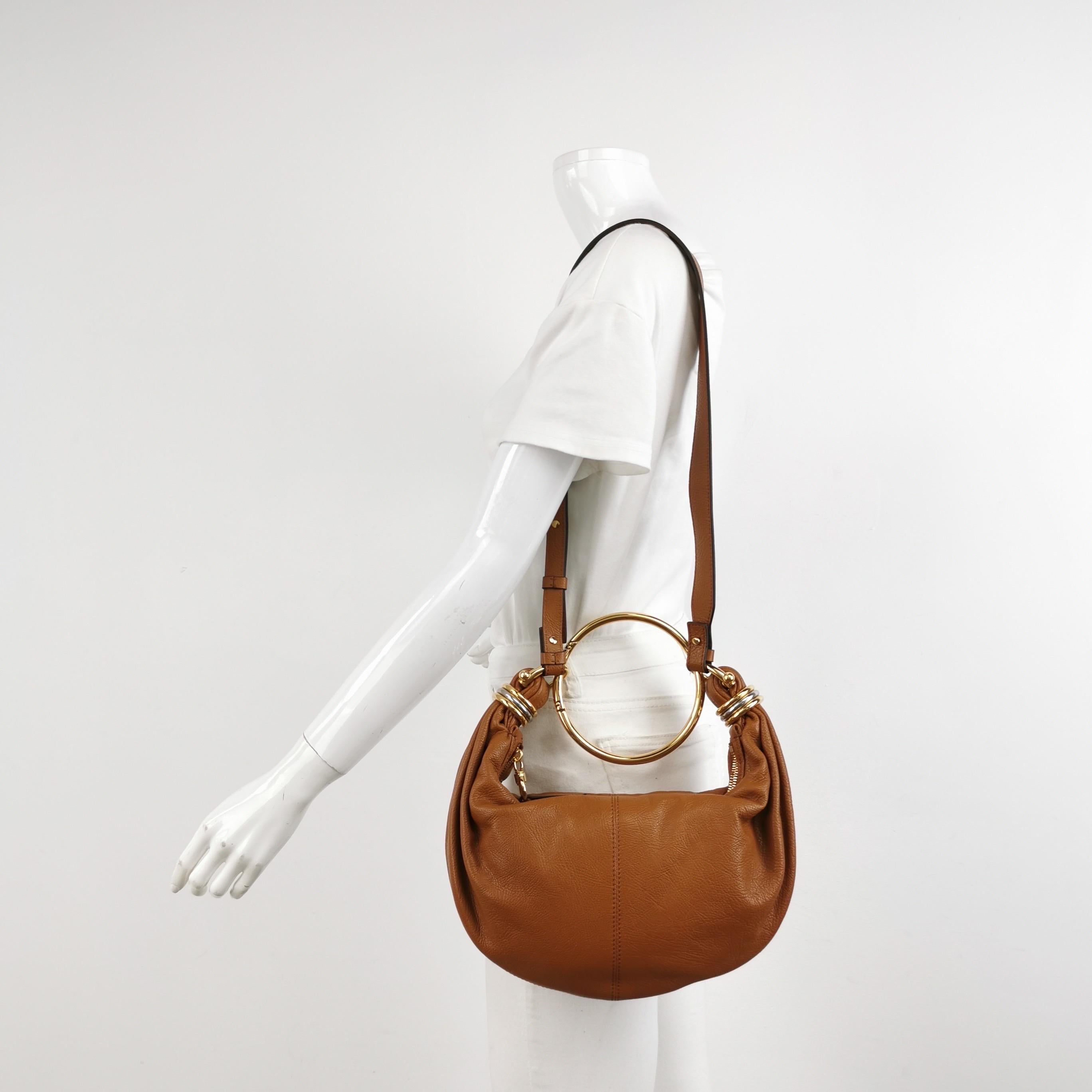 This CHLOÉ bag features a curved shape with a detachable bracelet top handle and stacked mixed-metal rings. Made in Italy from glossed textured-leather, it offers ample space for your phone, cardholder and lip gloss. Use the shoulder strap for