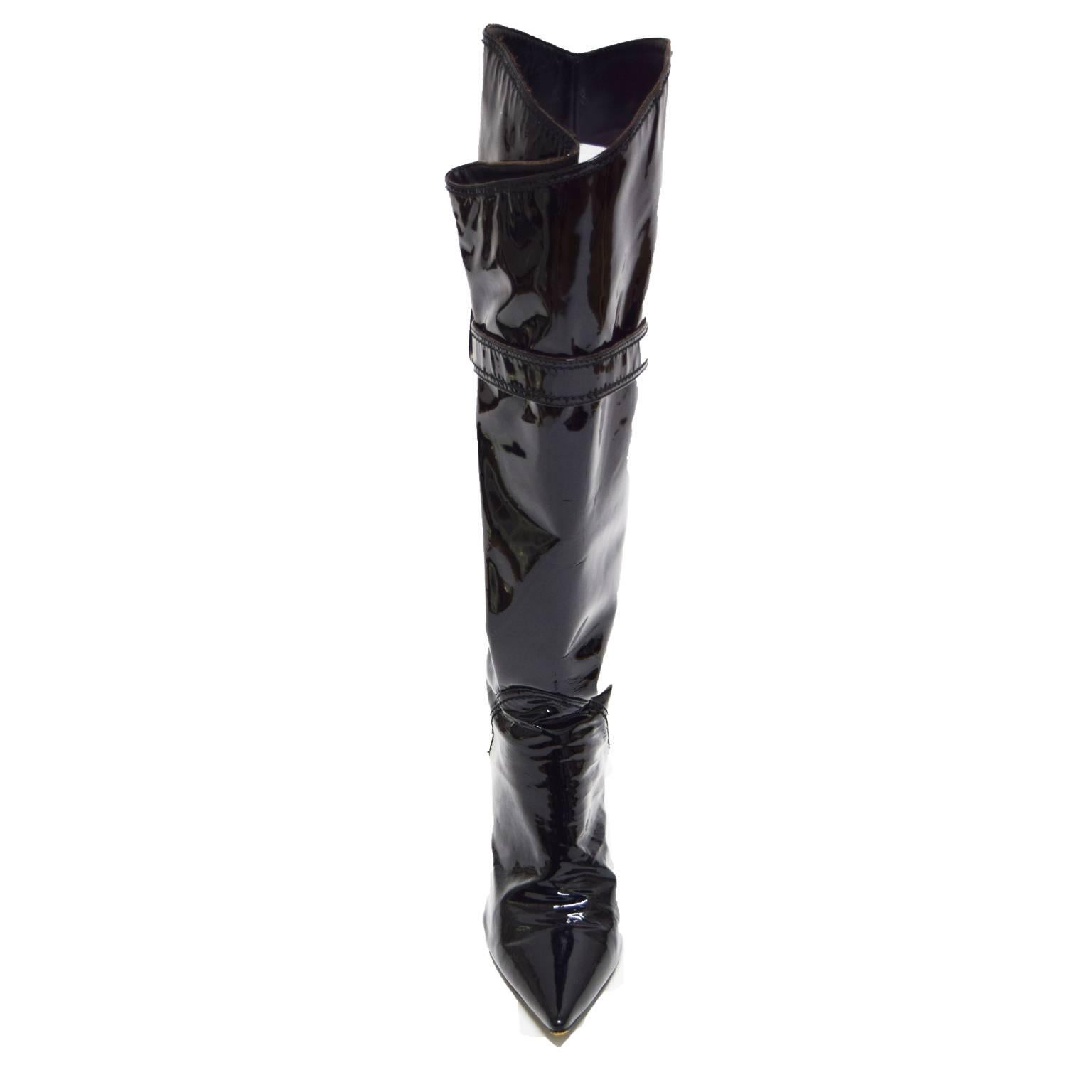 These sexy boots by Sergio Rossi, are made of black patent leather and have a front flap that pleats on the outside when buckled by strap. The toe is pointed and the heel is 3.5 in inches. The sole is textured leather and the shaft hits right below