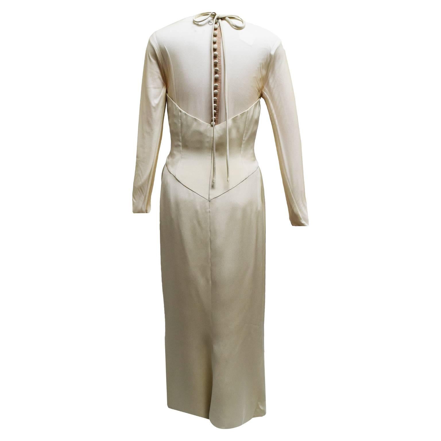 This beautiful gown by Vera Wang is made out of beige satin and is fully lined. The dress is a elegant sheath dress with empire waist and a jeweled neckline.  The dress is long sleeved, and the back has a delicate buttoned closure, a satin neck tie,