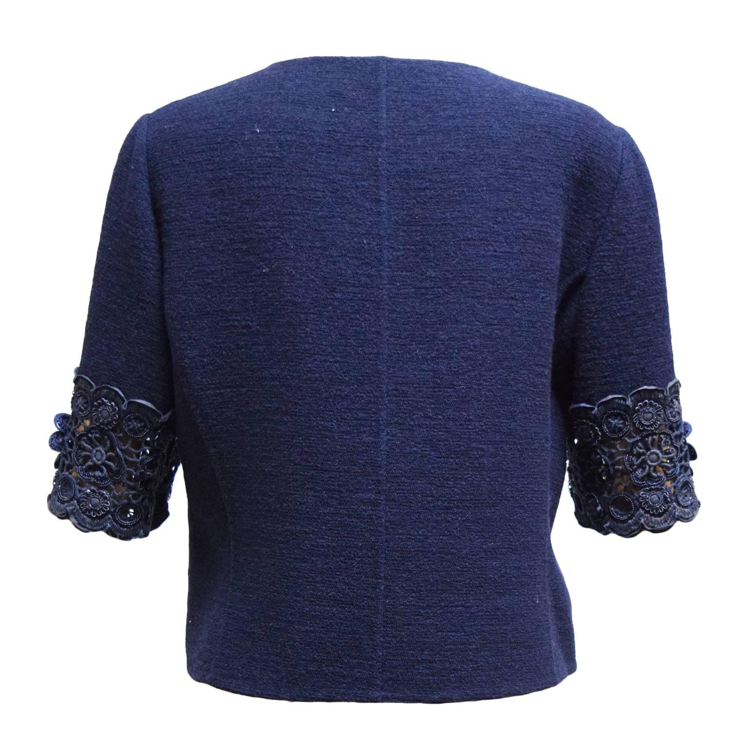 This Oscar de la Renta cardigan is navy blue wool and has floral embroidery along the bust and the bodice. It is short sleeved and has snap closures. 