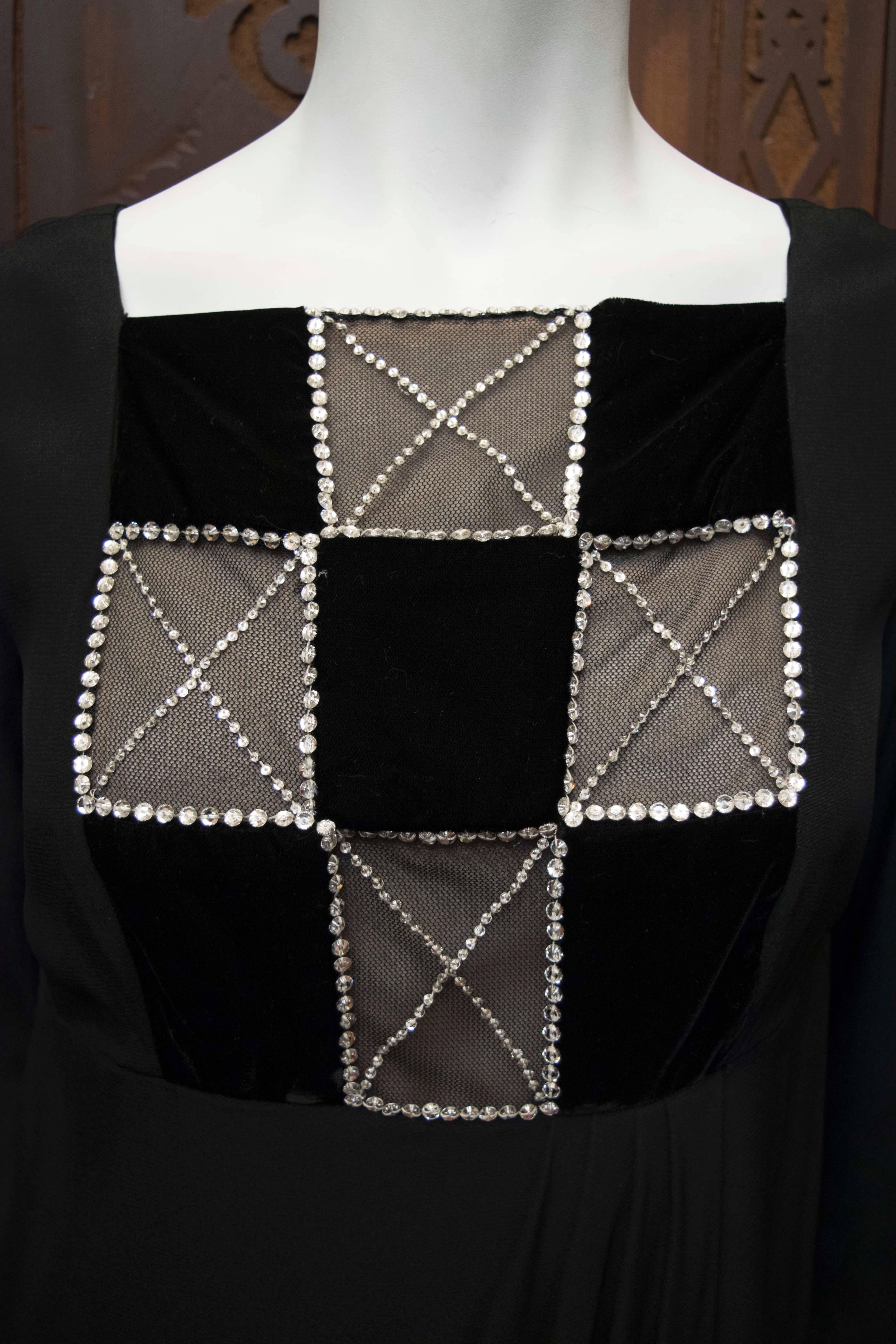 1980s Bob Mackie long sleeve black crepe cocktail dress with rondel crystal trimmed illusion bodice featuring contrasting squares of nude net over lining. Sleeve is gathered at shoulder. Skirt of dress is gathered at the front in a neat grecian