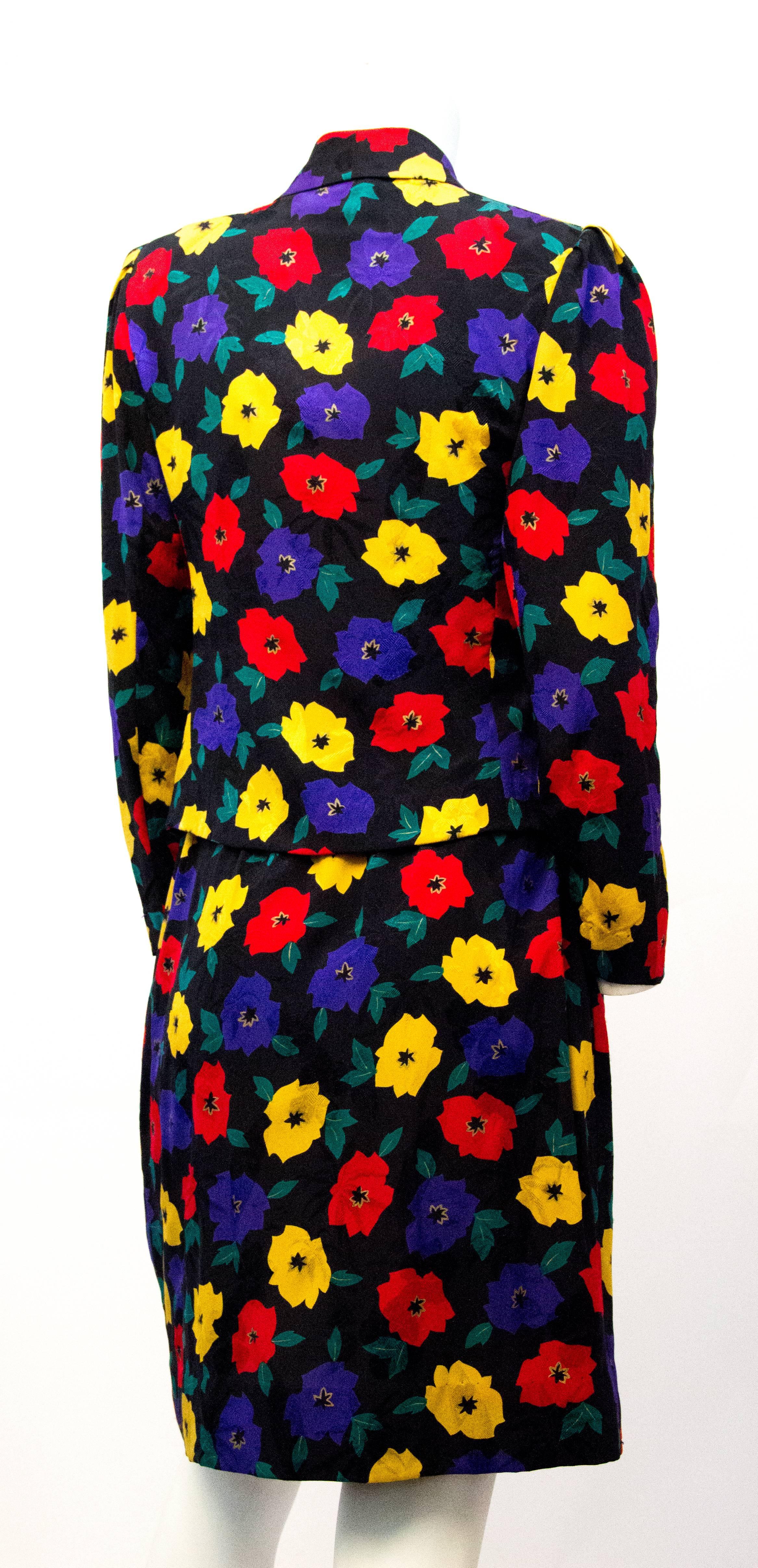 80s Emanuel Ungaro black silk jacquard suit with colorful floral print. Jacket has shoulder pads. Buttons and hooks up the front. Skirt wraps around and fastens with one button at the hip. Set is unlined. 