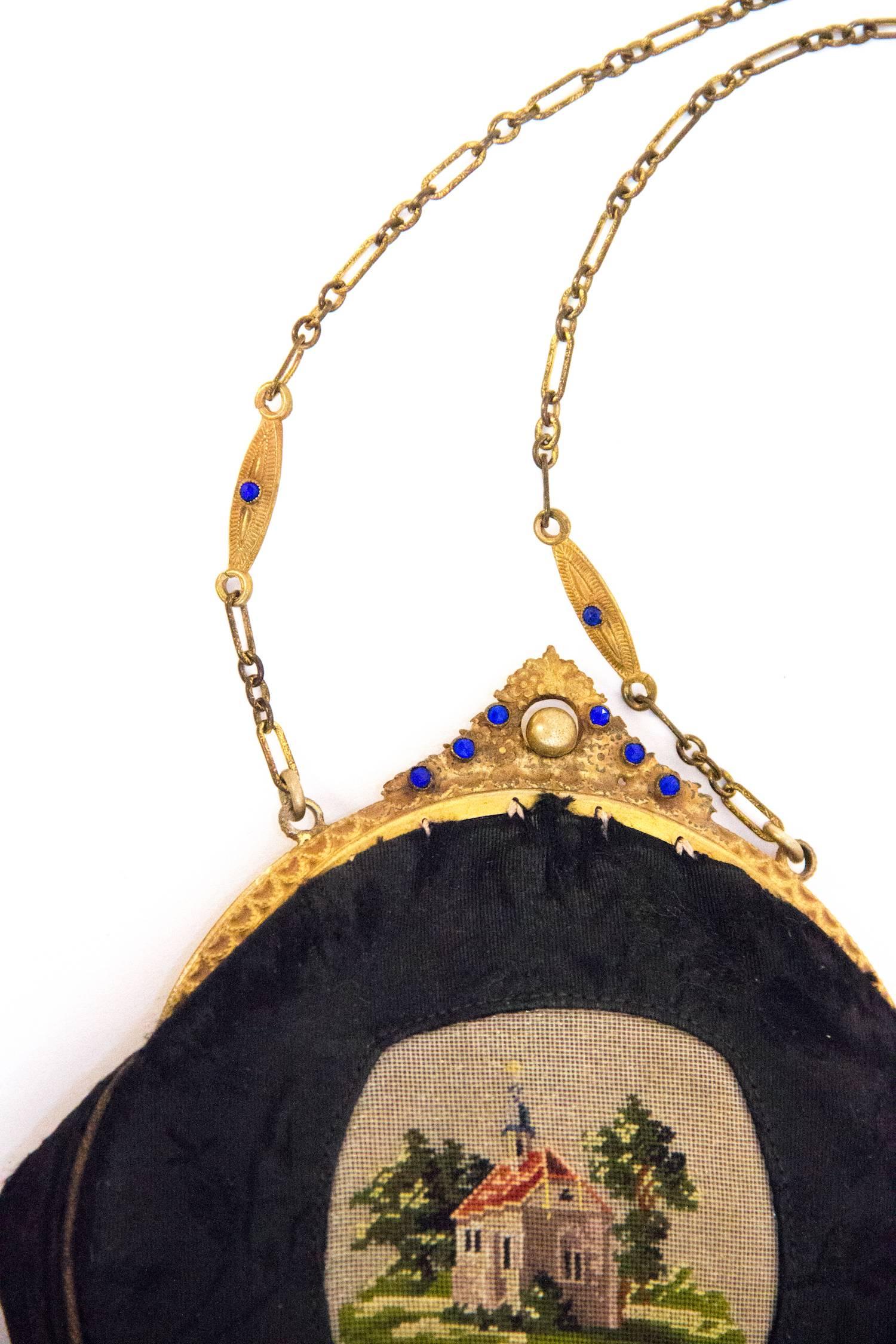 Edwardian black jacquard pouch purse with petit point scene of a house and trees. Gold toned metal frame with blue glass embellishments. Original interior small round mirror that is attached with a small chain. Roughly lined in cream colored cotton.