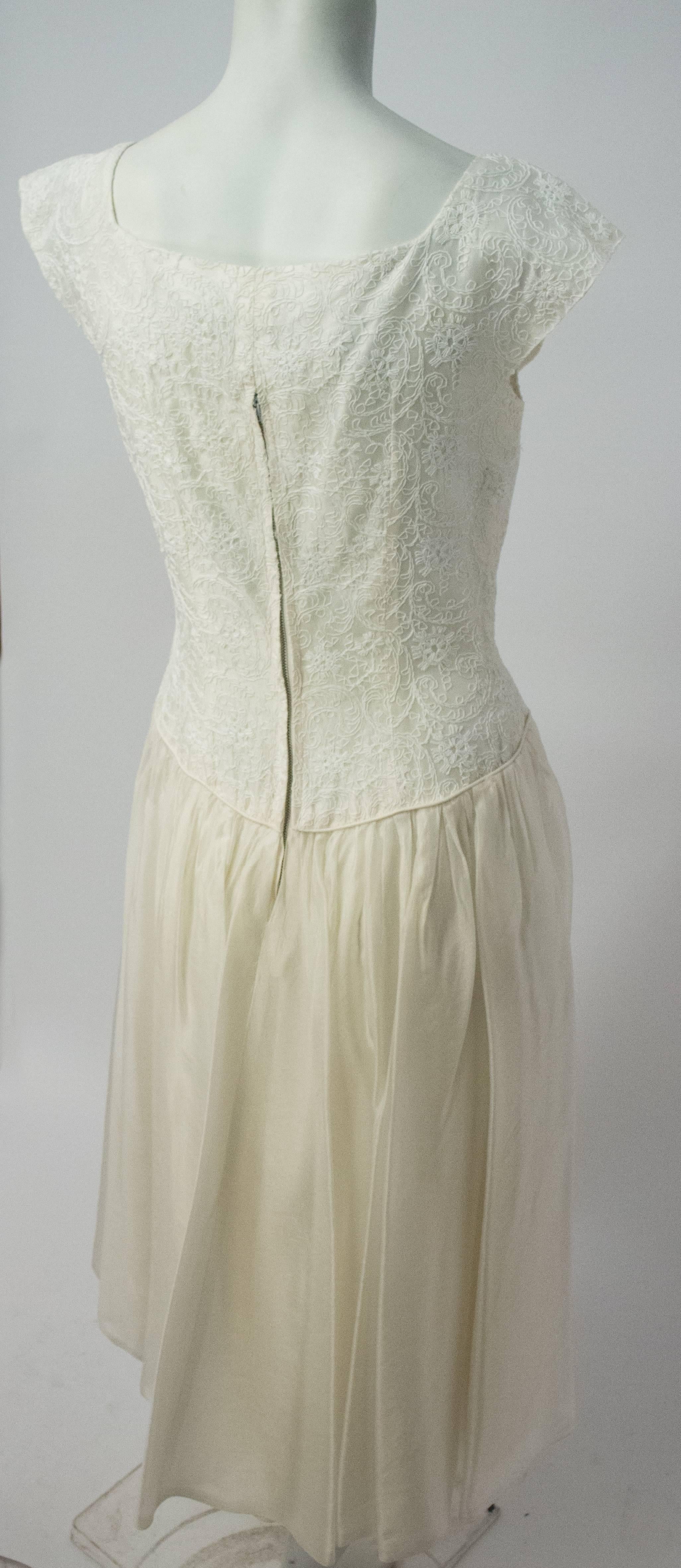 robe Emma Domb des années 50 en organza brodé blanc. Fausse ouverture à boutons sur le devant. Fermeture éclair arrière en métal. 