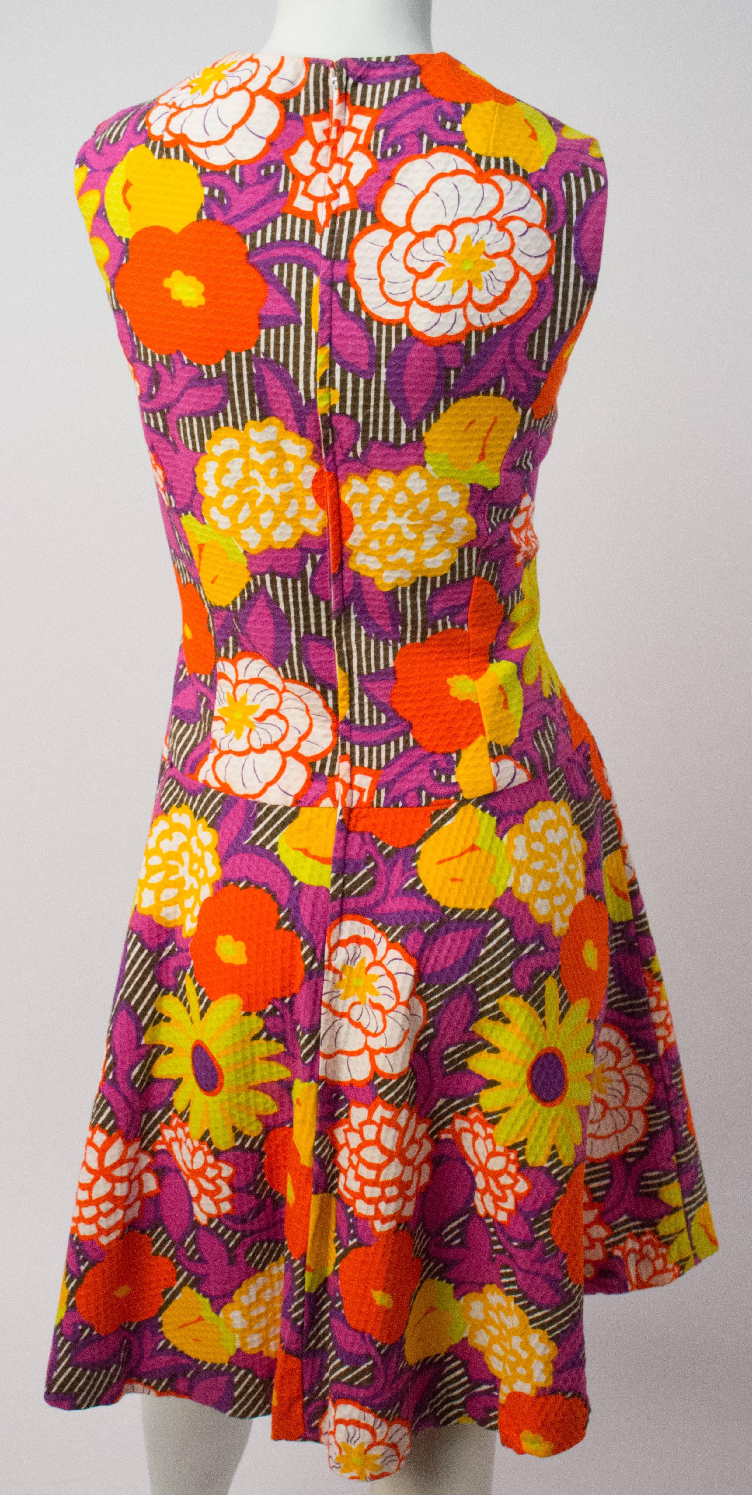 60s Flower Power Drop-Waist Dress. Bright florals printed on a textured waffle weave. Two front patch pockets. Back zipper closure. 