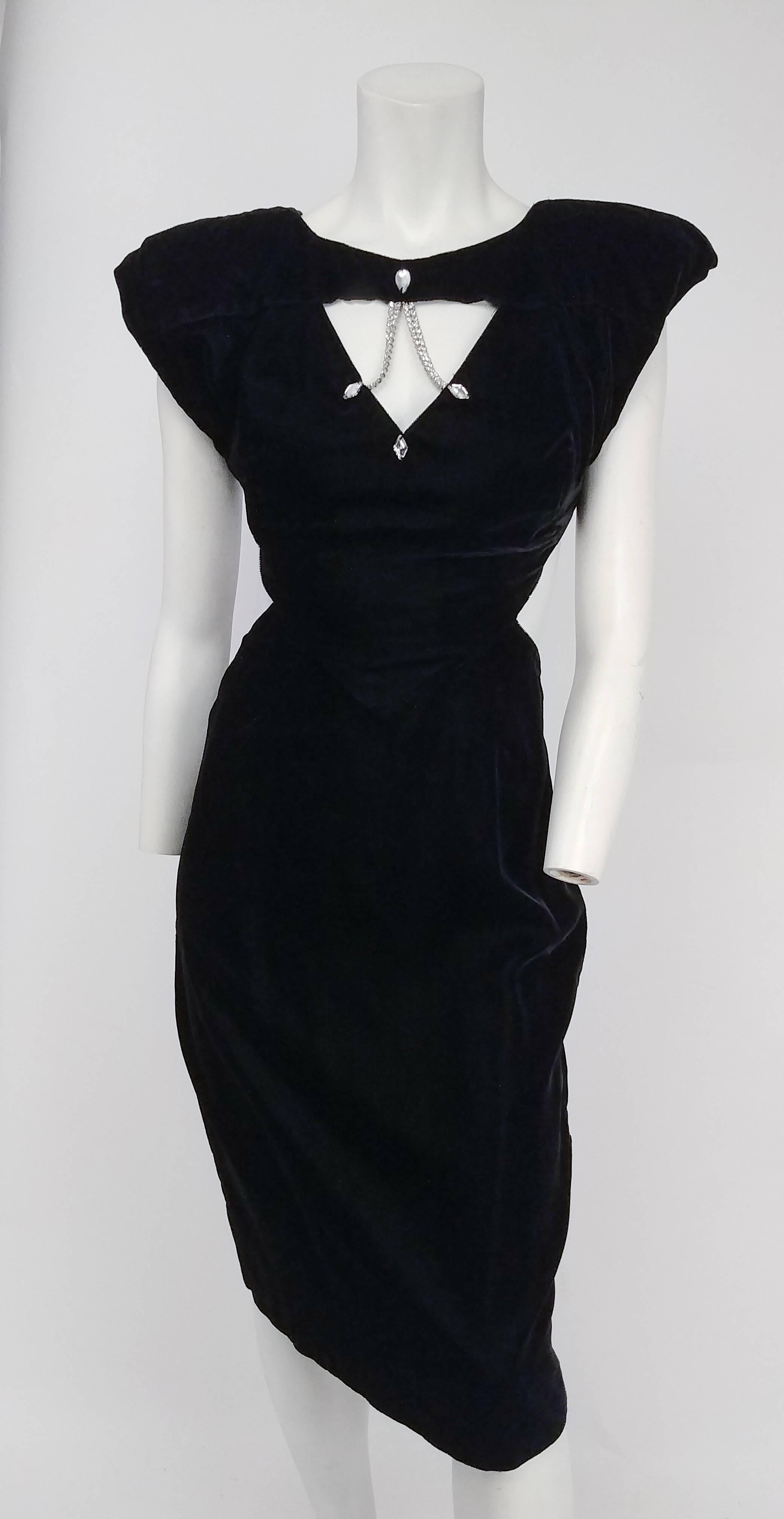 1980s Black Velvet Open Back Cocktail Dress. Front bodice has cutout detail embellished with rhinestones. Sides and back are open, with buckles to hold dress in place. Shoulders are padded. Buckles make size adjustable. 