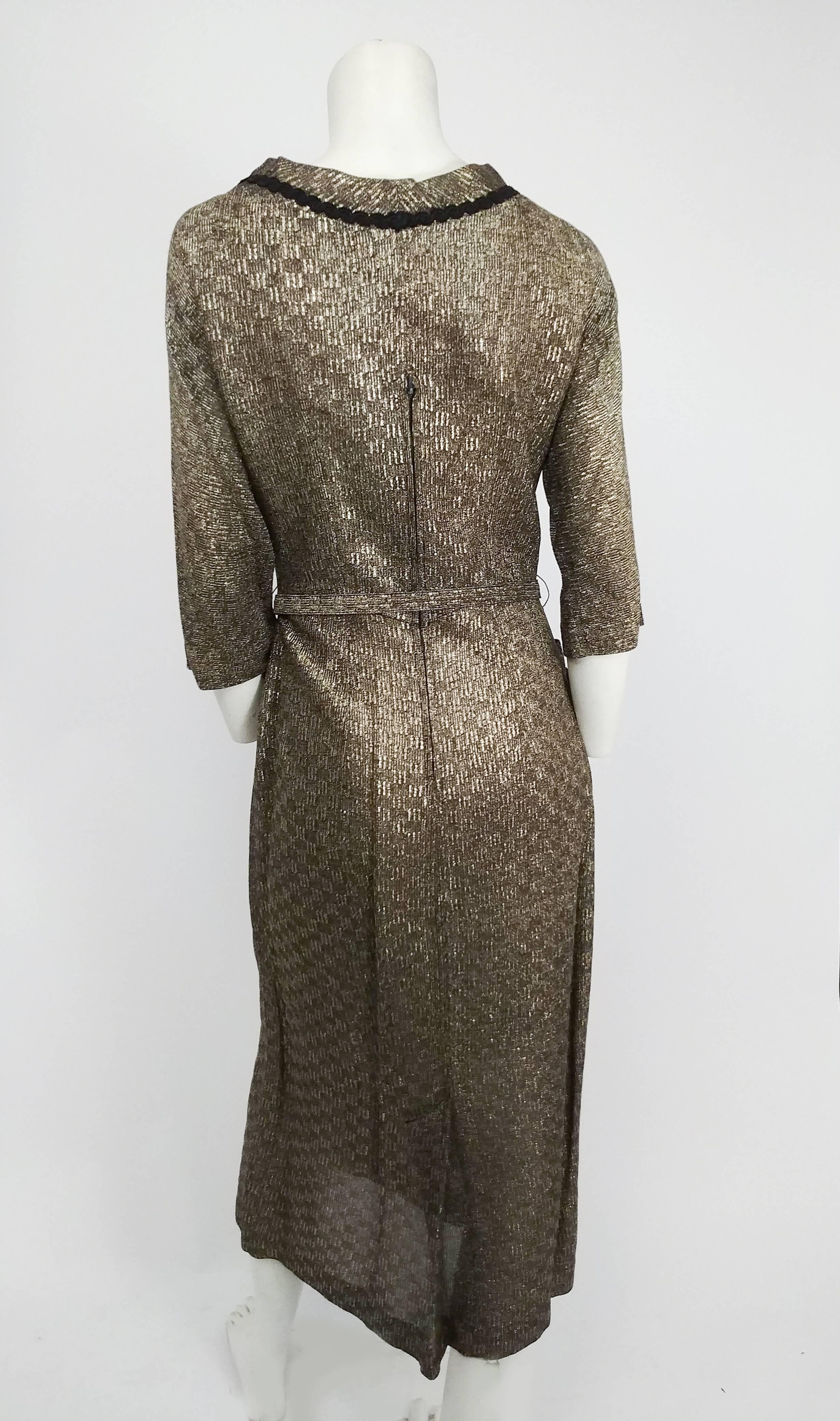 1940s Gold Lamé Dress. Black braid trim on collar and hips and adorable tassel detail on boat neck collar. Zips up mid back. Glove length sleeves. Original belt included. 