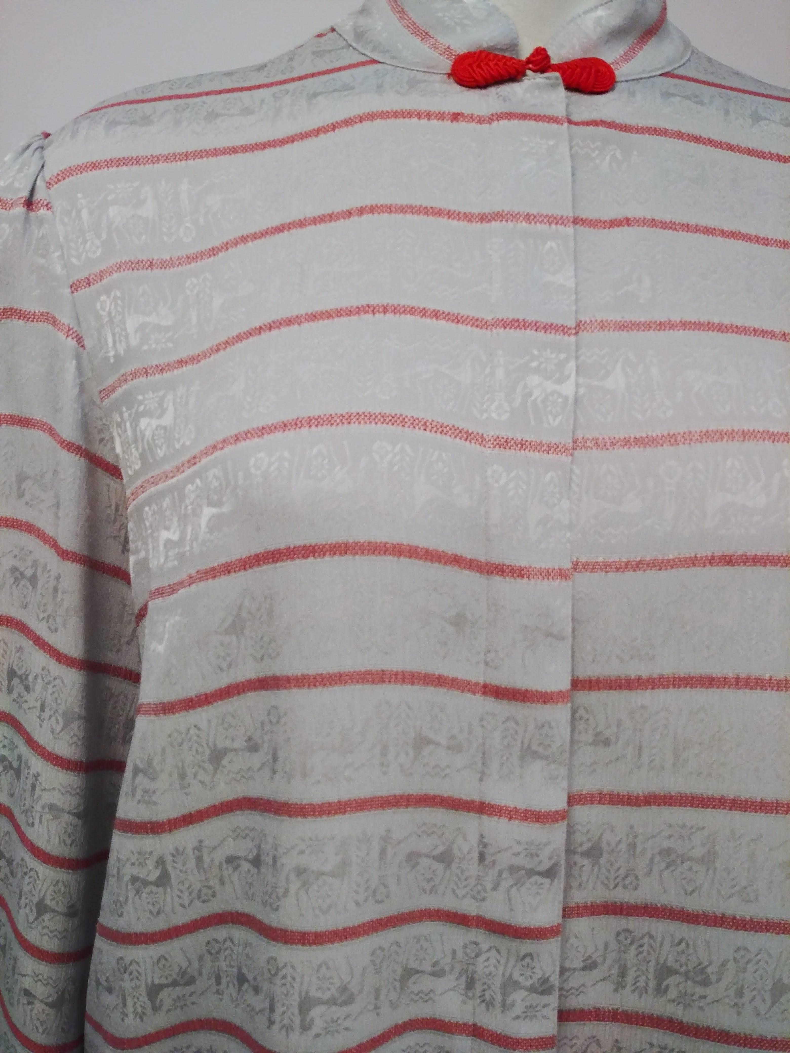 1980s Silk Jacquard Silver Blouse w/ Mesopotamian Motifs. Silver fabric with red stripes with Mesopotamian designs woven into fabric. Red frog clasp at neck, hidden button placket. Unlined, slightly padded shoulders for a puffed sleeve look. 