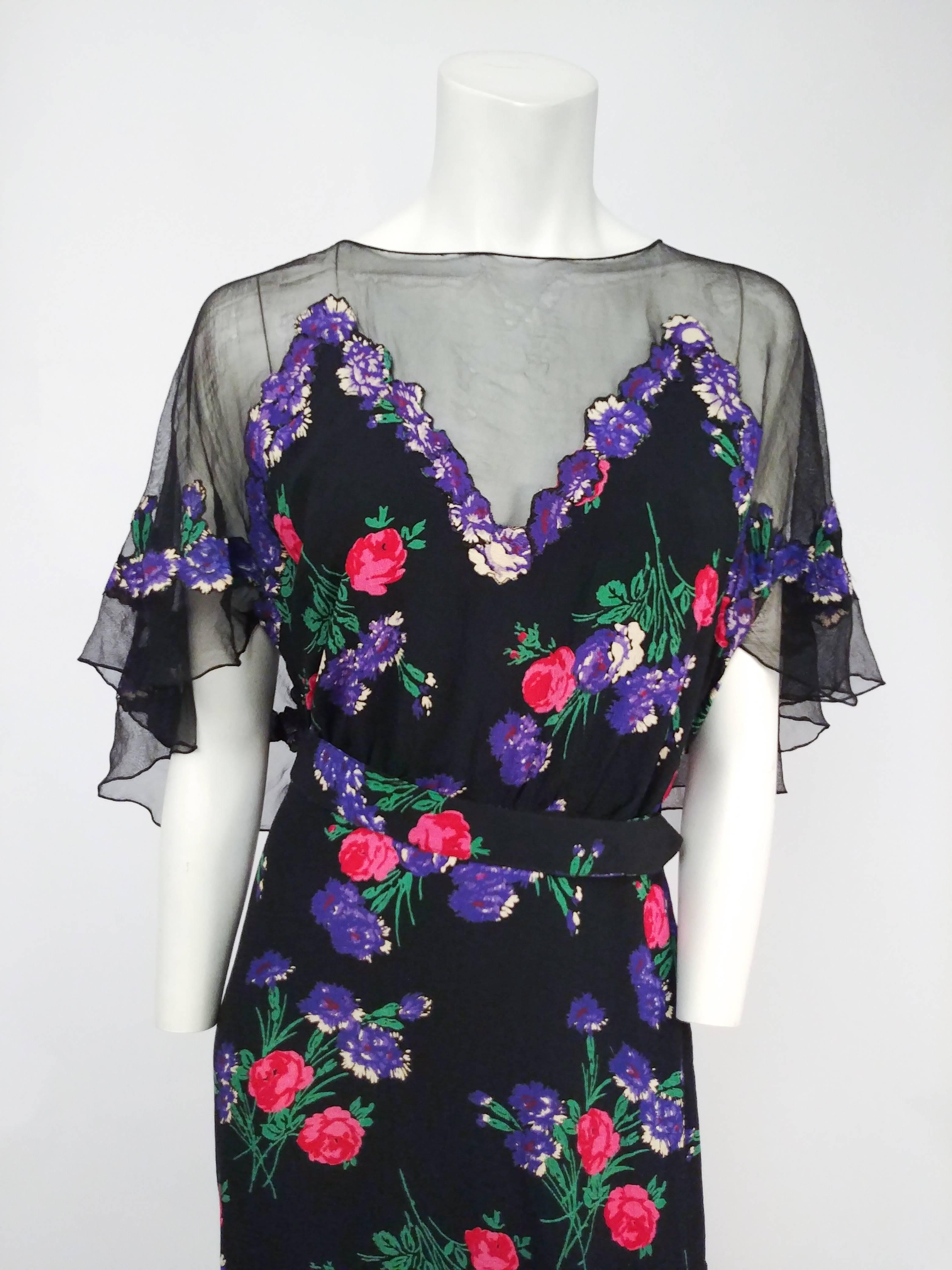 robe en maille noire imprimée de fleurs des années 1930. Robe en maille transparente avec application de fleurs découpées, caplet intégré au dos. Ceinture attachée. 