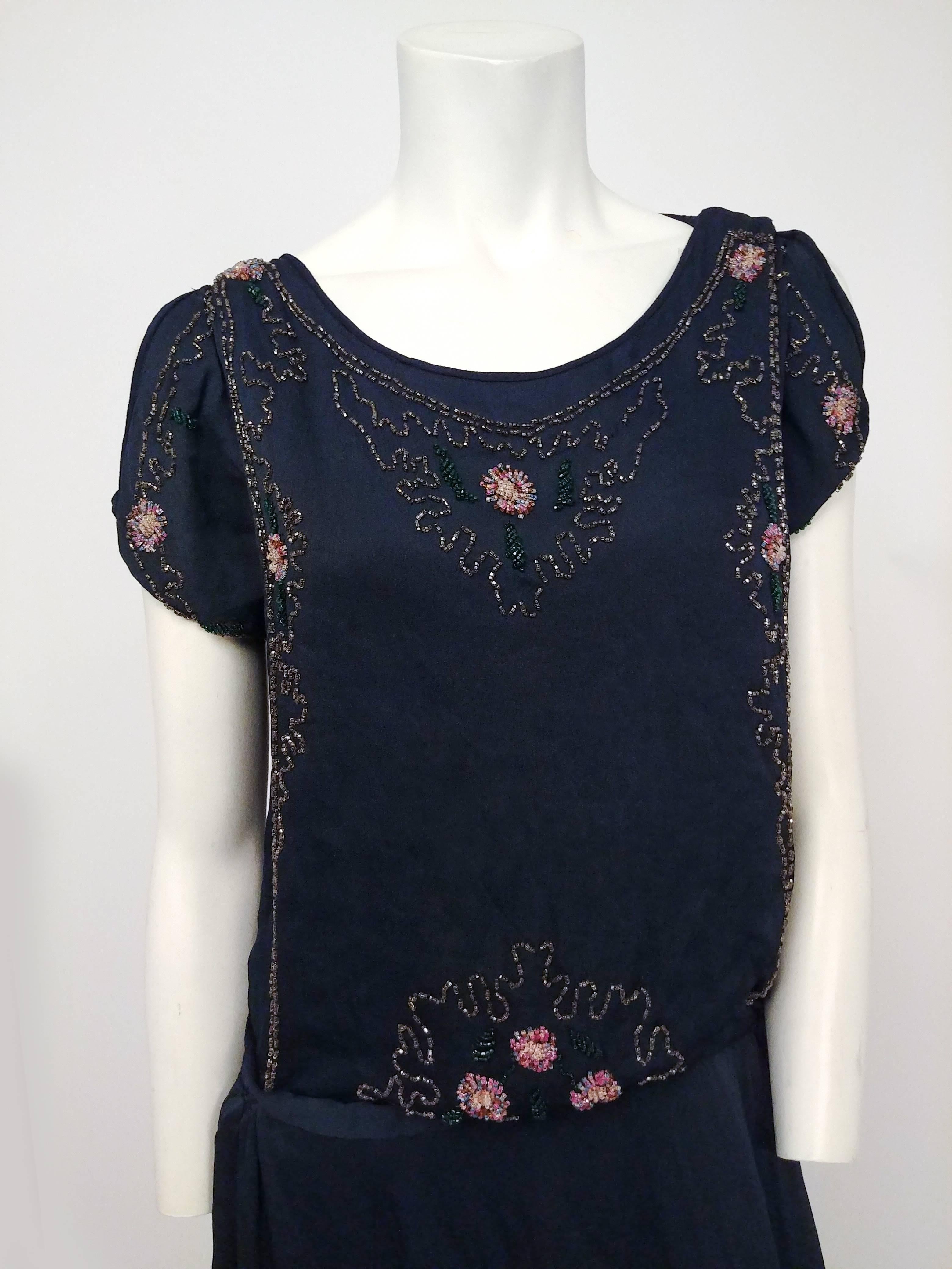 1920s Black Silk Beaded Dress. Black silk crepe embroidered with beads in a floral motif. Open shoulder, ties at sides of hips for a drop-waist silhouette. Scalloped hem. No closures, slips on over head. Lined. 