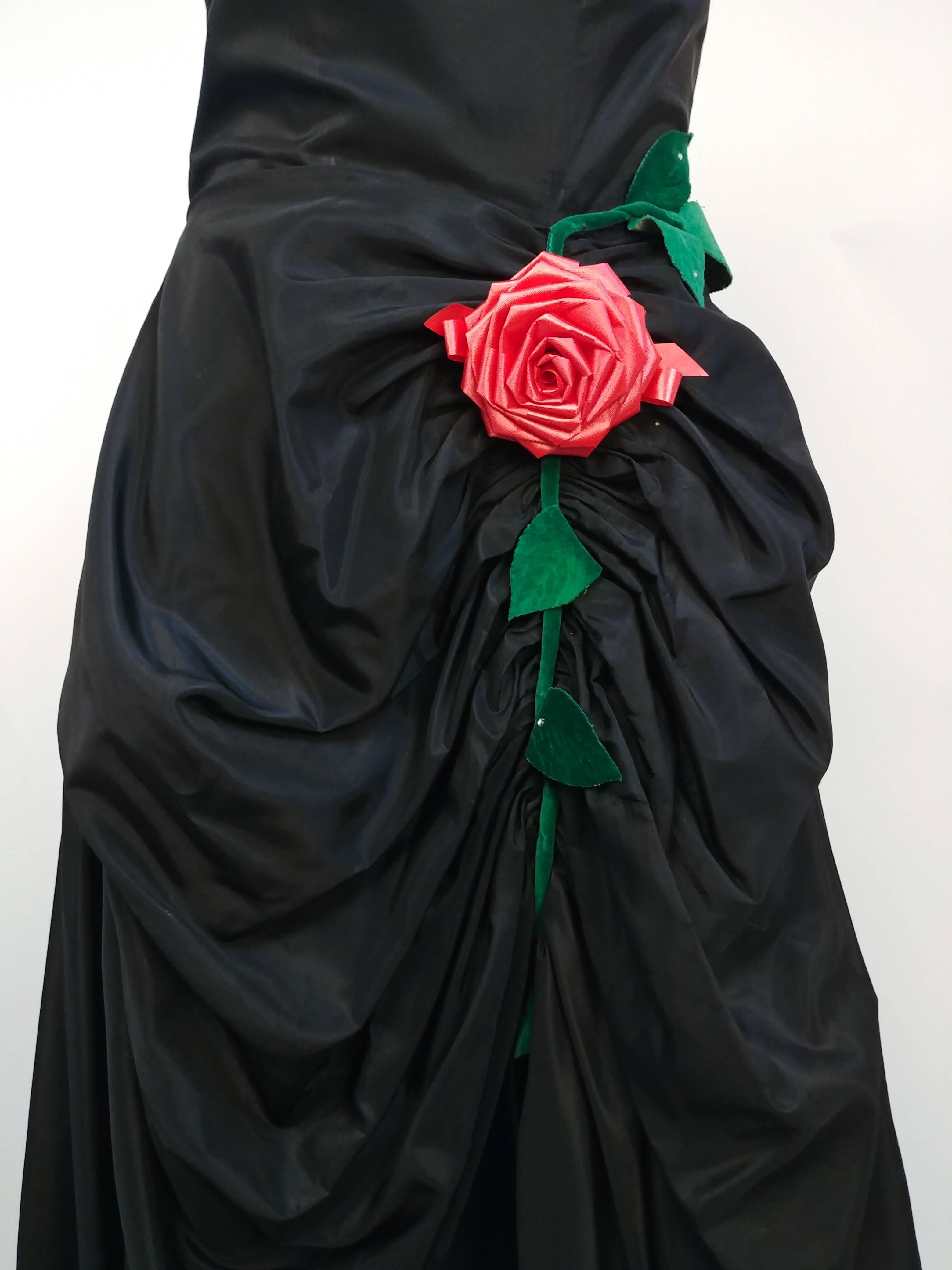 1950s Black Ruched Front Rose Embellishment Gown. Black taffeta fabric drapes down the front beautifully to create dimension and drama in this floor-length, stunning gown, further embellished with a single large ribbon rose and velvet leaves.